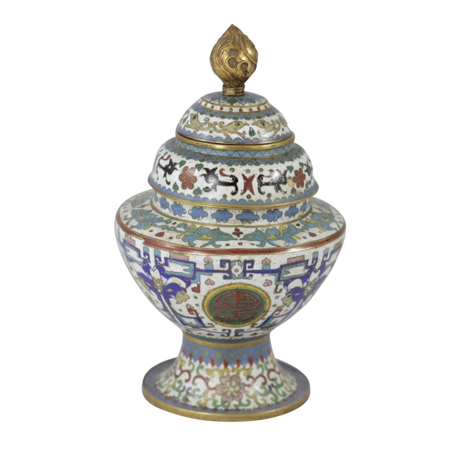 This cloisonné vessel from early 20th century, China is a curious vase made up of three separate chambers. Its colorful design in red, blue and green covers the white base with brass detailing and finial.