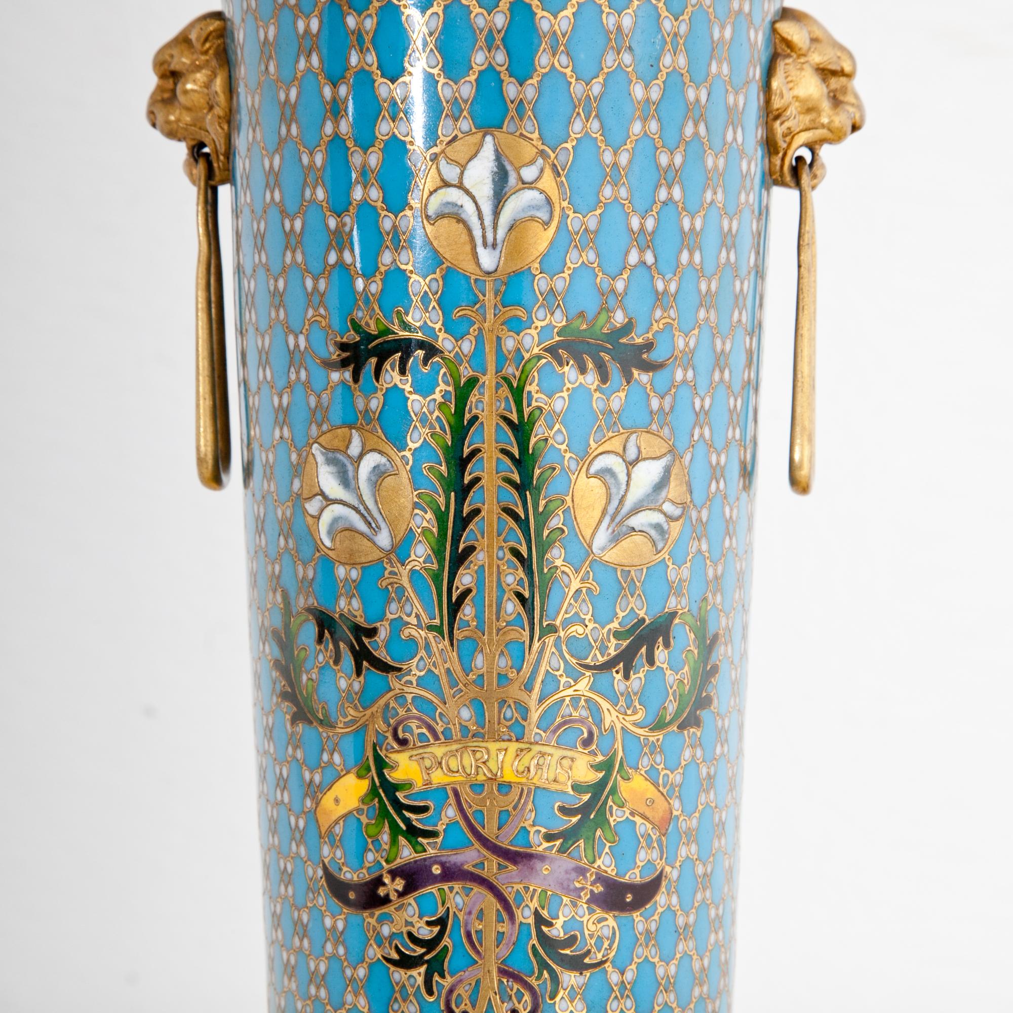 Cloisonné Vase signed Barbedienne of the second half of the 19th century. The tulip shaped body stands on four legs and has lateral lion head handles. The cloisonné work shows white lilies on a blue ground with a golden rhomboid net pattern. Signed