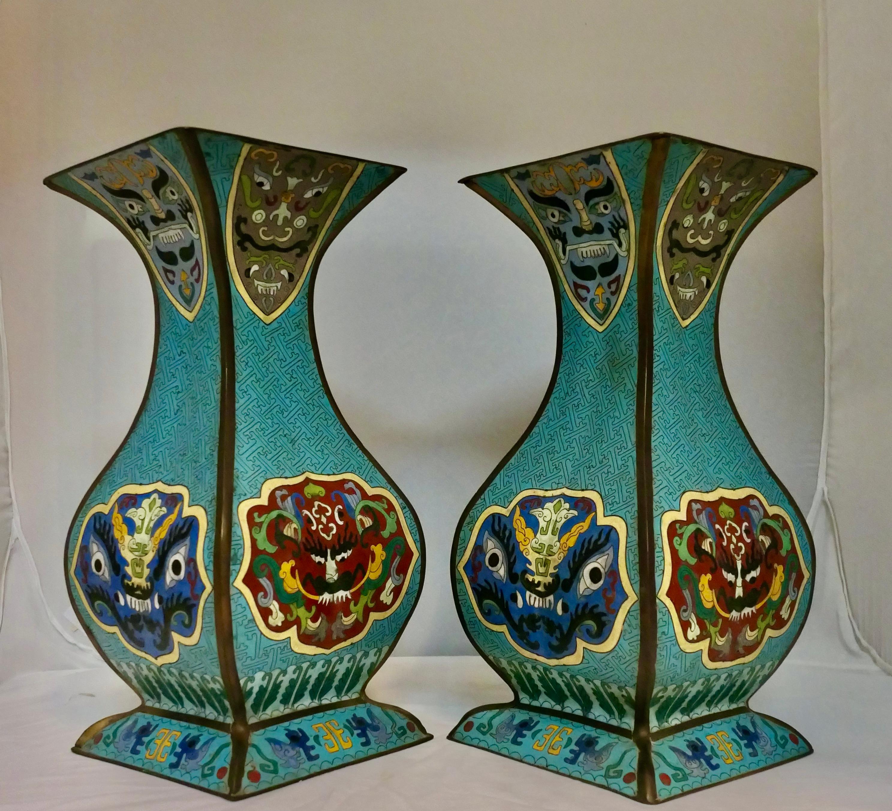 Cette paire de vases cloisonnés japonais du début du 20e siècle, décorés à la main, présente un design unique avec un corps incurvé à quatre panneaux, accentué par une base à jupe allongée. Chaque vase est décoré de superbes fonds bleus avec