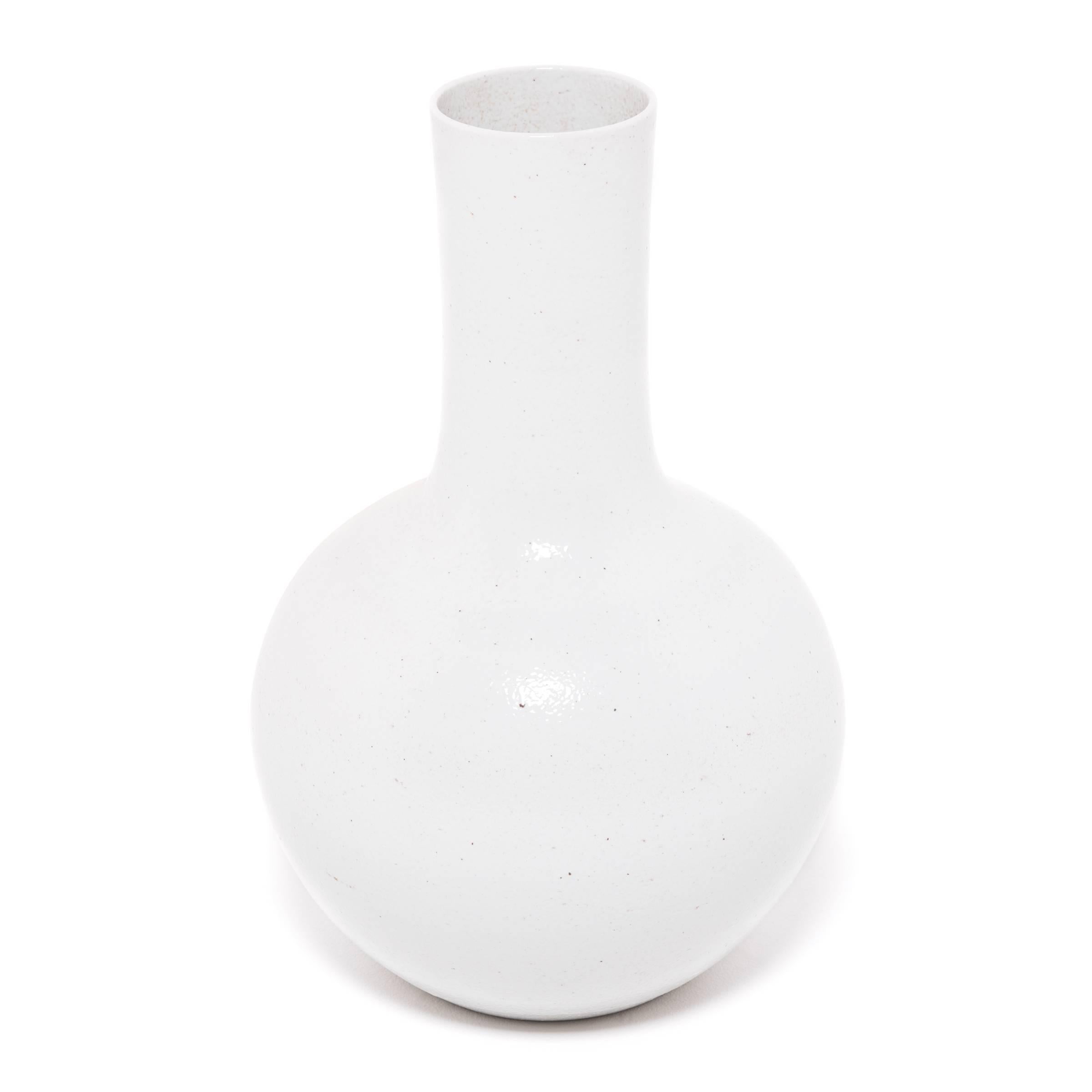 Drawing on a long Chinese tradition of ceramics, this striking long-necked vase is cloaked in an all-over milky white glaze. Sculpted by artisans in China's Zhejiang province, the large vase reinterprets a traditional shape known as a 