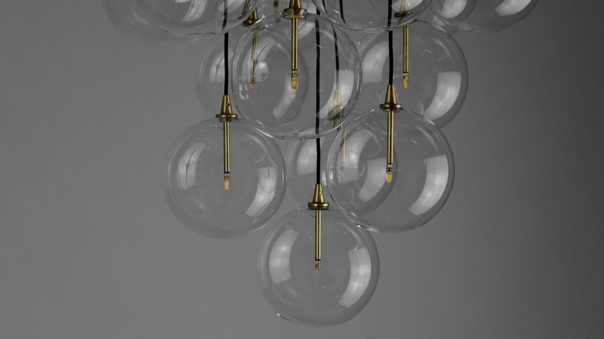 An arrangement of thirteen glass globes suspended from a discus of brass forms a serene ceiling constellation. The repeated sphere appears like a bundle of grapes, a tantalizing cluster floating in the air.

Available in our three signature