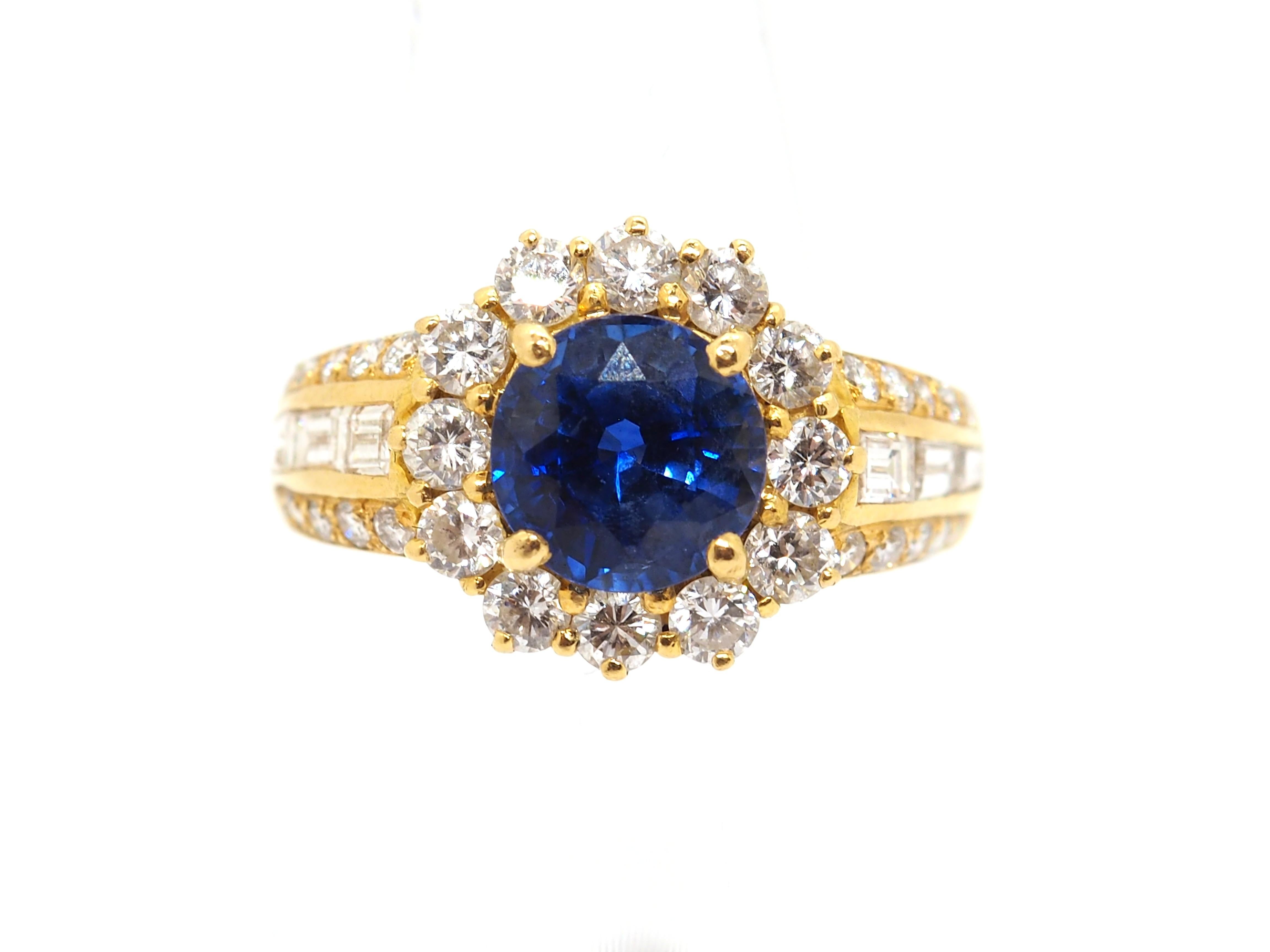 Beautiful cluster ring crafted in 18K yellow gold with a royal blue unheated and untreated round sapphire surrounded by a halo of round-cut brilliant diamonds with an approximate weight of 1 carat. Decorated also by the both sides with a round-cut