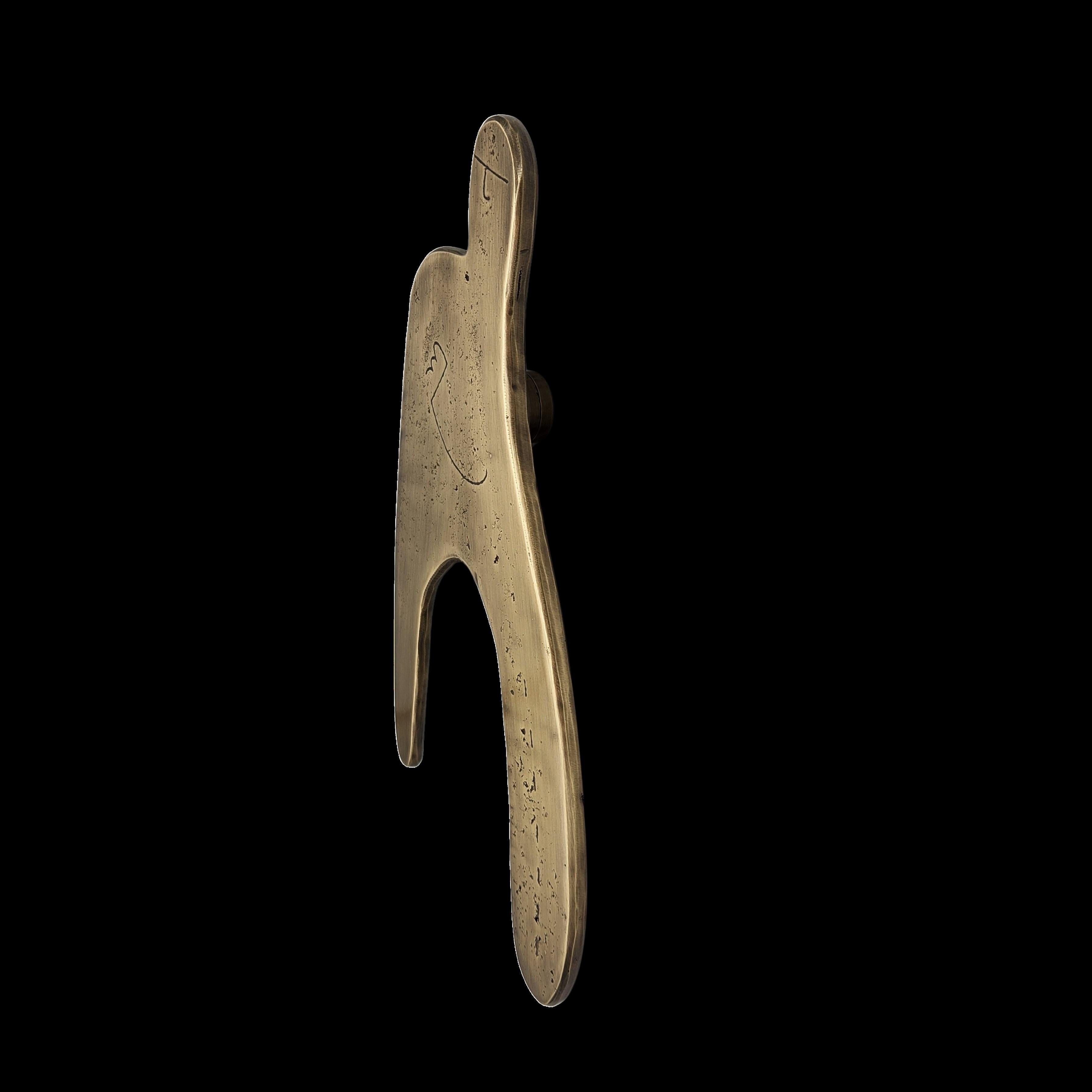 Este tirador de puerta de latón macizo presenta una silueta ancha y fluida, con líneas que sugieren una figura atrapada en un estado de desequilibrio controlado. La forma, a la vez ingenua y expresiva, se despliega con espontaneidad, animada por una