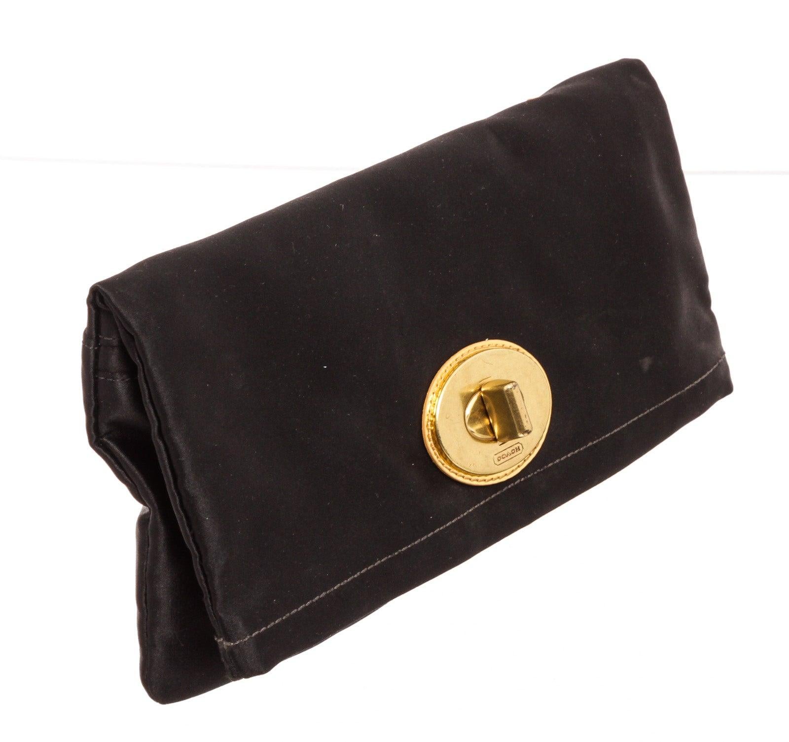 Coach black satin Amanda clutch with gold-tone hardware, logo placard at front, french purse pouch at back, two compartments under flap with zip closure, purple satin interior lining, and overall flap closure.
25094MSC