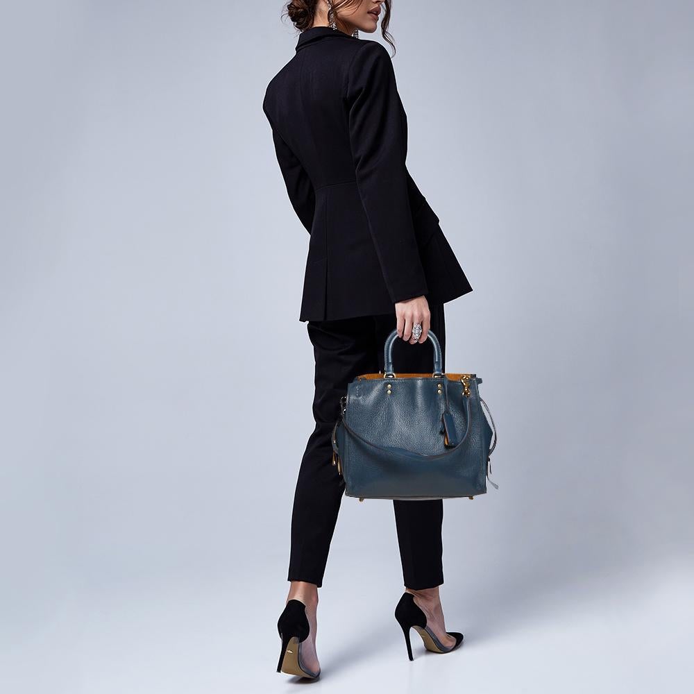 This beauty is crafted from leather in a timeless blue hue. This Coach piece has a spacious suede interior housing a zipper pocket. This Rogue tote features two top handles, protective metal feet, and a turn-lock secured leather tag to the front.

