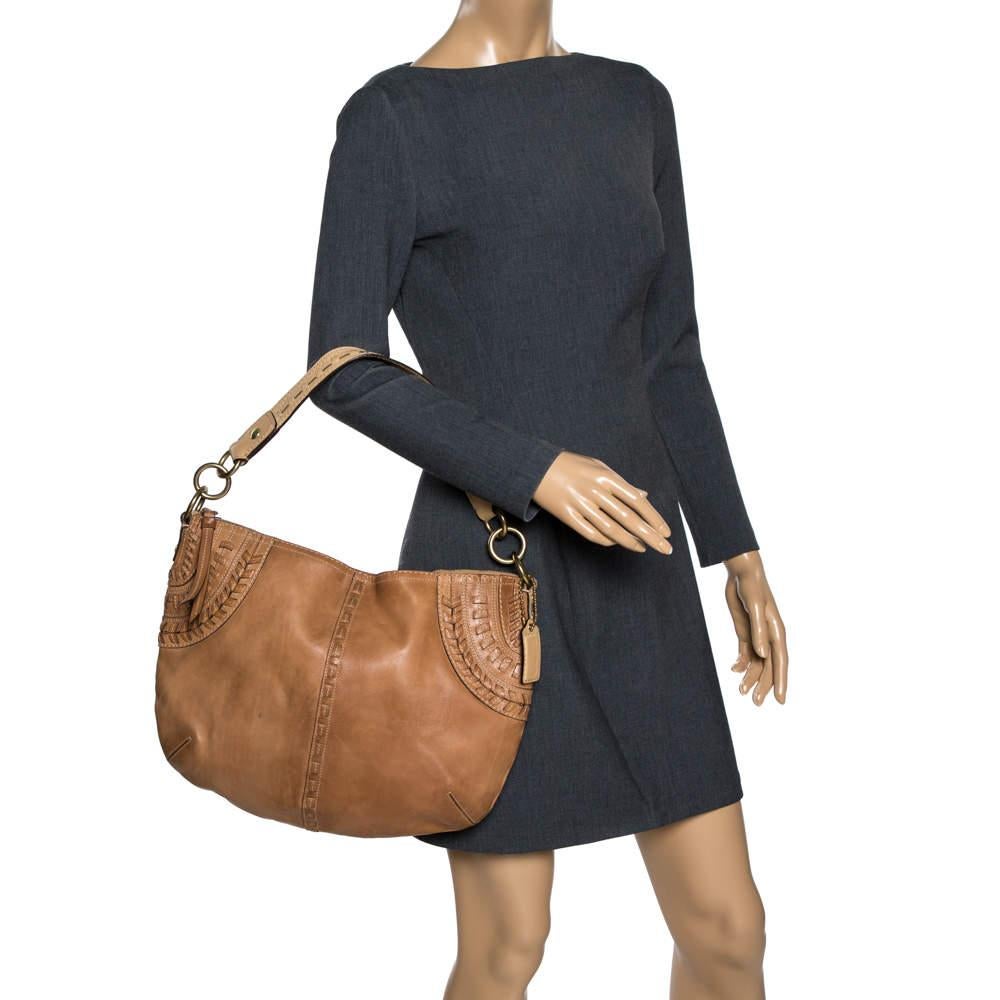 This stylish Coach hobo bag is perfect for everyday use. Crafted meticulously from quality leather, it comes in a versatile shade of brown. It has a single handle, stitch detailing on the exterior, a zip closure that opens to a fabric-lined interior