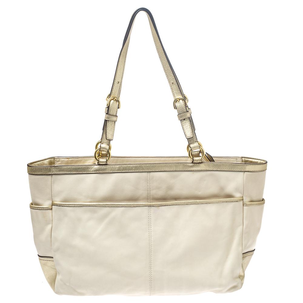 This tote from Coach is crafted from quality leather and comes in lovely hues of cream white & metallic gold. It is accompanied by a gold-tone logo detail on the front. Two handles are provided for you to carry it, and a spacious satin-lined