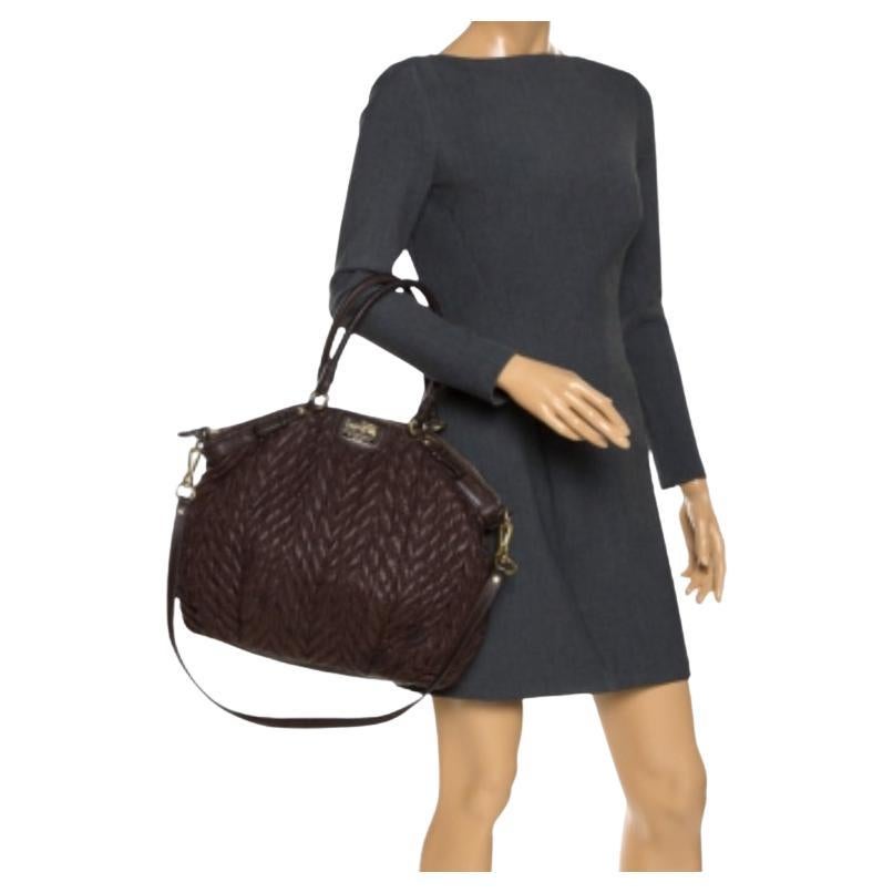 Favolosa ed elegante, questa borsa Madison di Coach è qui per affascinare tutti! Questa creazione marrone scuro è realizzata in pelle e presenta dettagli di trapuntatura. Sfoggia un doppio manico superiore, una tracolla e il logo del marchio sul