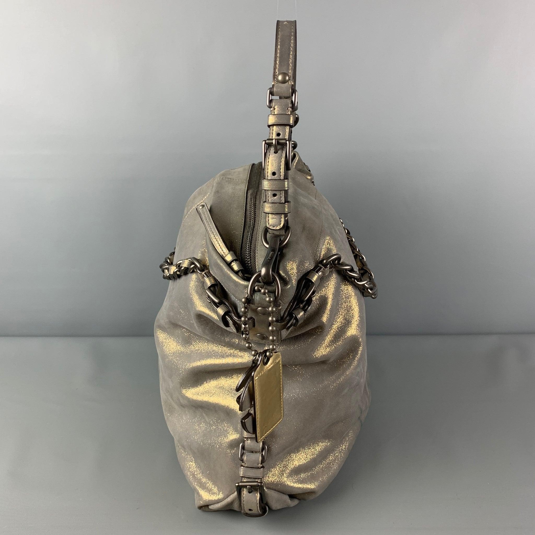 Le sac COACH est présenté dans un cuir gris métallisé avec des accessoires de couleur argentée, des poignées supérieures à maillons, une bandoulière réglable, des breloques avec logo, des fentes intérieures et une fermeture à glissière sur le