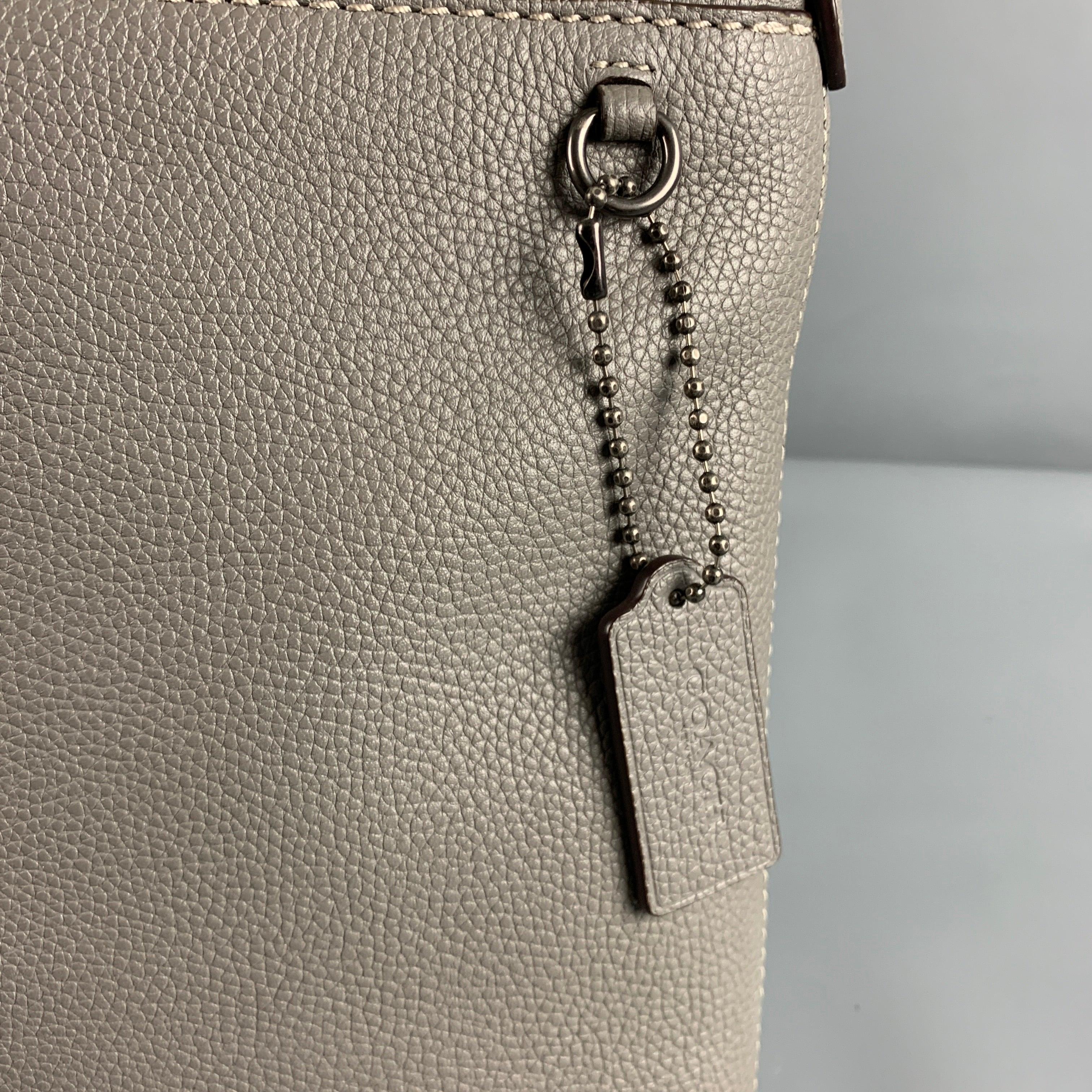 COACH handbag
in a grey leather featuring a pebble grain texture, contrasting black adjustable strap, gunmetal tone hardware, and zip closure.Very Good Pre-Owned Condition. Minor mark on front and strap. 

Measurements: 
  Length: 10 inches Width: 1