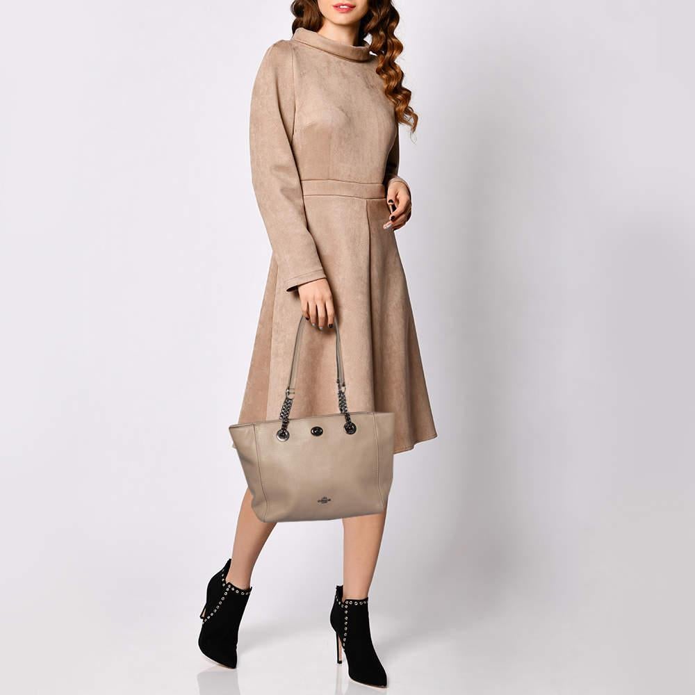 Flaunt this tote by Coach, crafted from quality leather. It comes in a grey shade that adds a touch of elegance and subtlety. It is styled with dual handles, a turn-lock in black-tone, a spacious interior with a zip pocket and slip pockets. It is