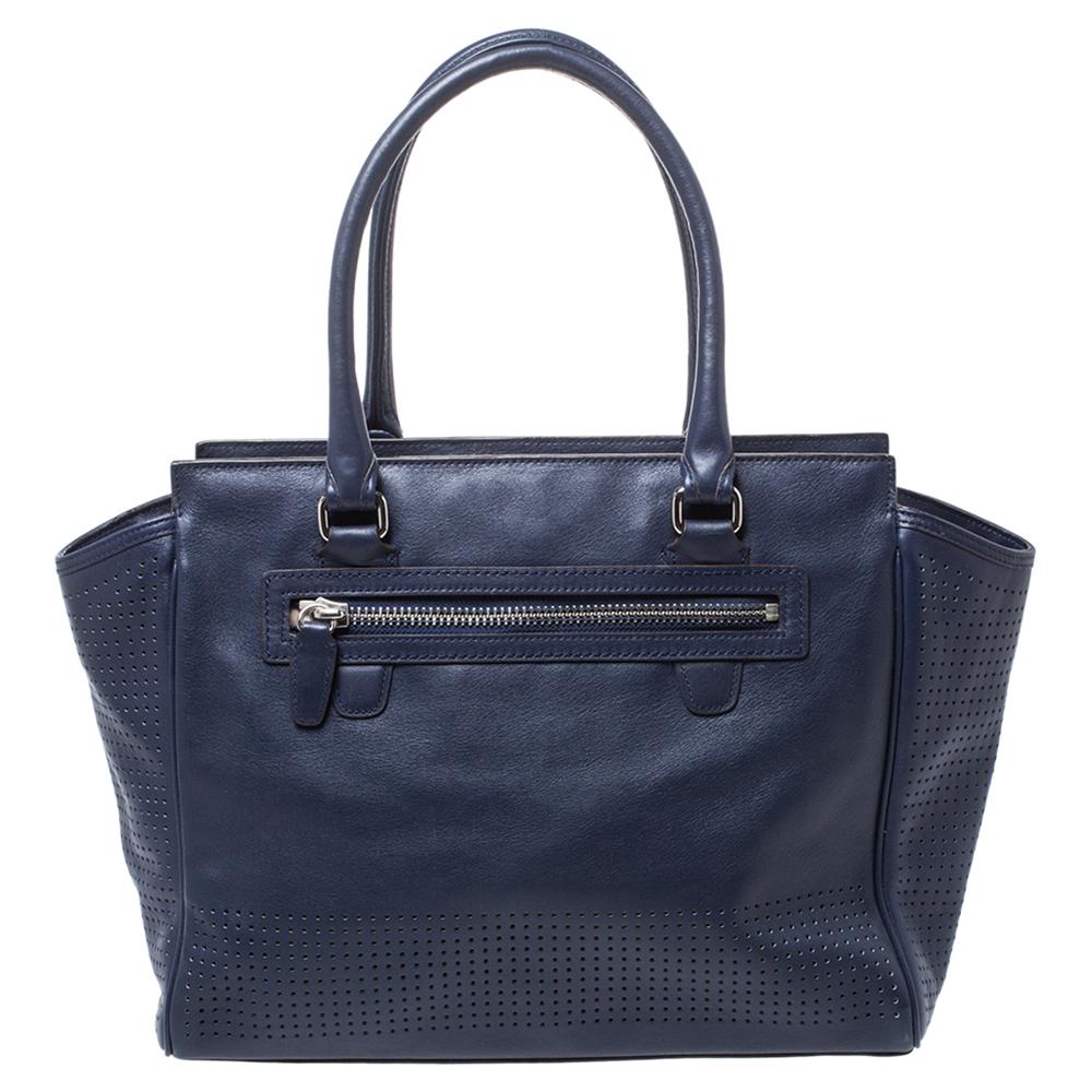 This beautiful Candace Carryall tote bag from Coach is highly functional while being charming and stylish. Crafted from perforated leather, the navy blue & green bag features dual handles and silver-tone hardware. The canvas-lined interior comes