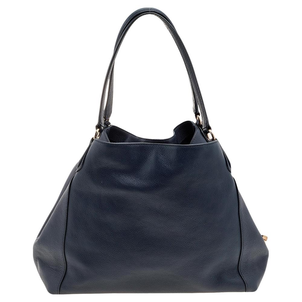 From the House of Coach, here comes this stunning Edie shoulder bag, which will grant you nothing but style and practicality. It is made from navy-blue leather on the exterior and flaunts gold-toned hardware. The spacious fabric-lined interior of