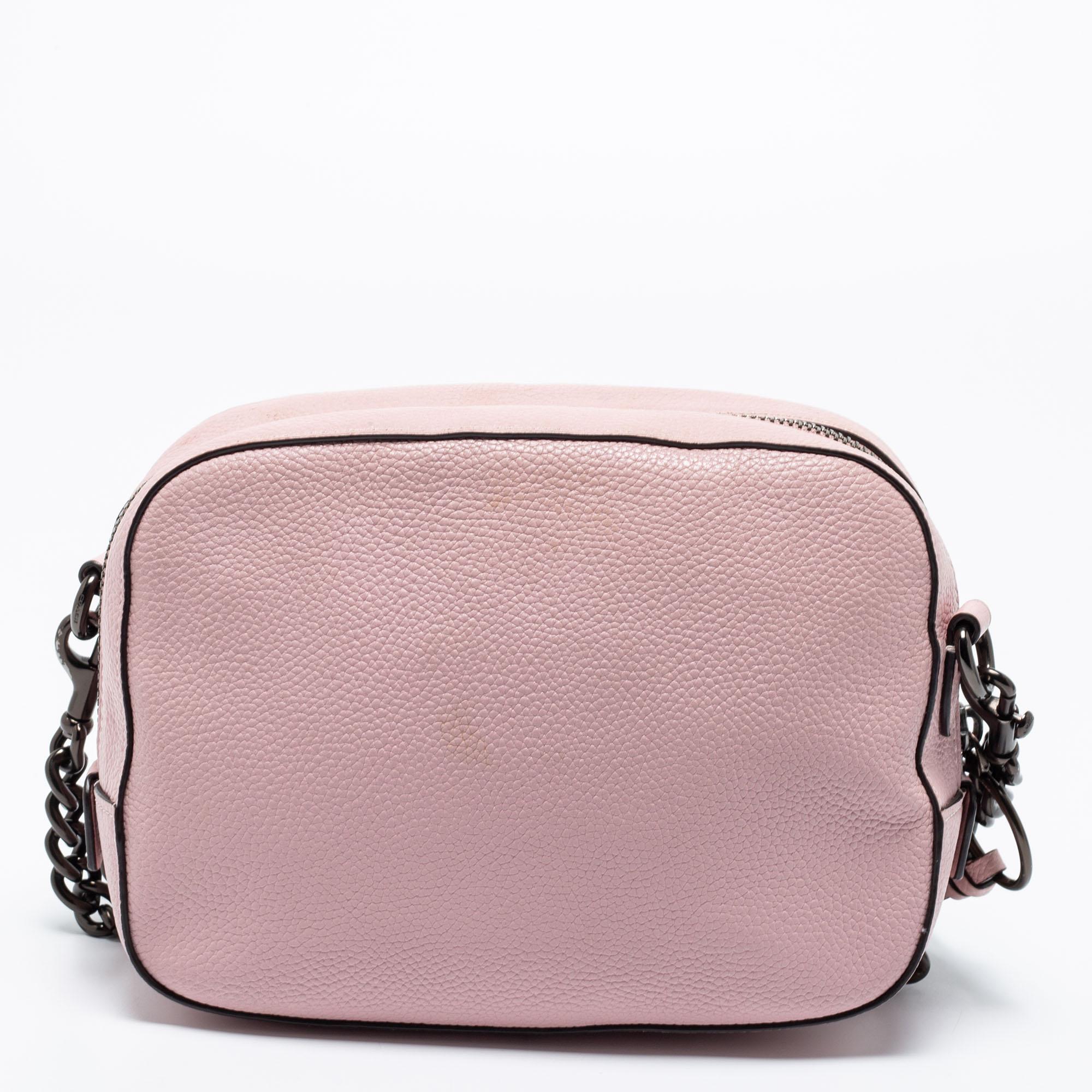 Elegance meets luxury in this Camera shoulder bag from the House of Coach. It is created using pink pebbled leather, with a logo motif perched on the front. It features a fabric-lined interior, black-tone hardware, and a sturdy strap. This bag will