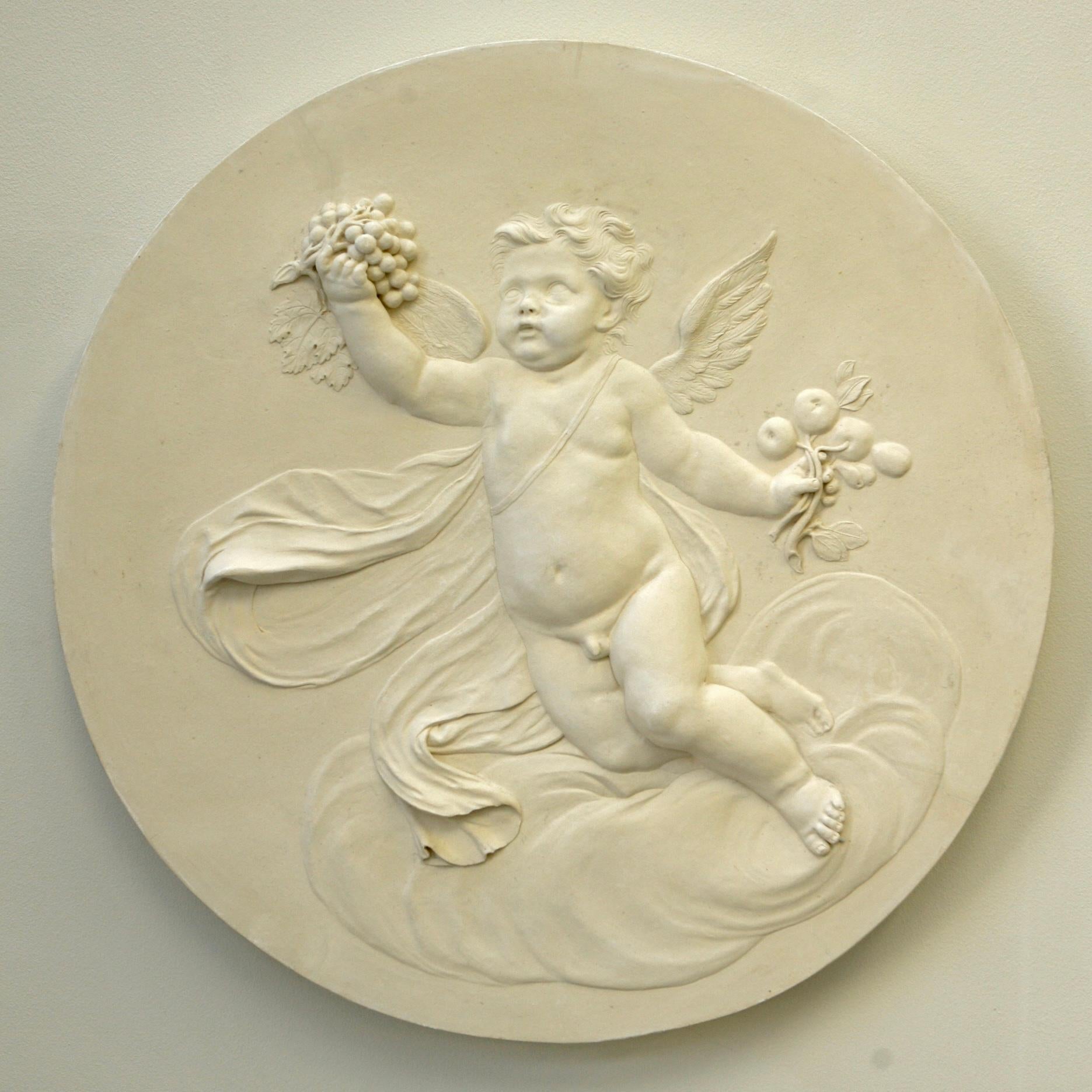 Rondelle décorative du Studio Coade représentant un chérubin "Automne" flottant sur une formation nuageuse. L'automne est décoré d'une abondance de fruits. Modelé en bas-relief délicat. Les rondeaux des quatre saisons sont influencés par les motifs