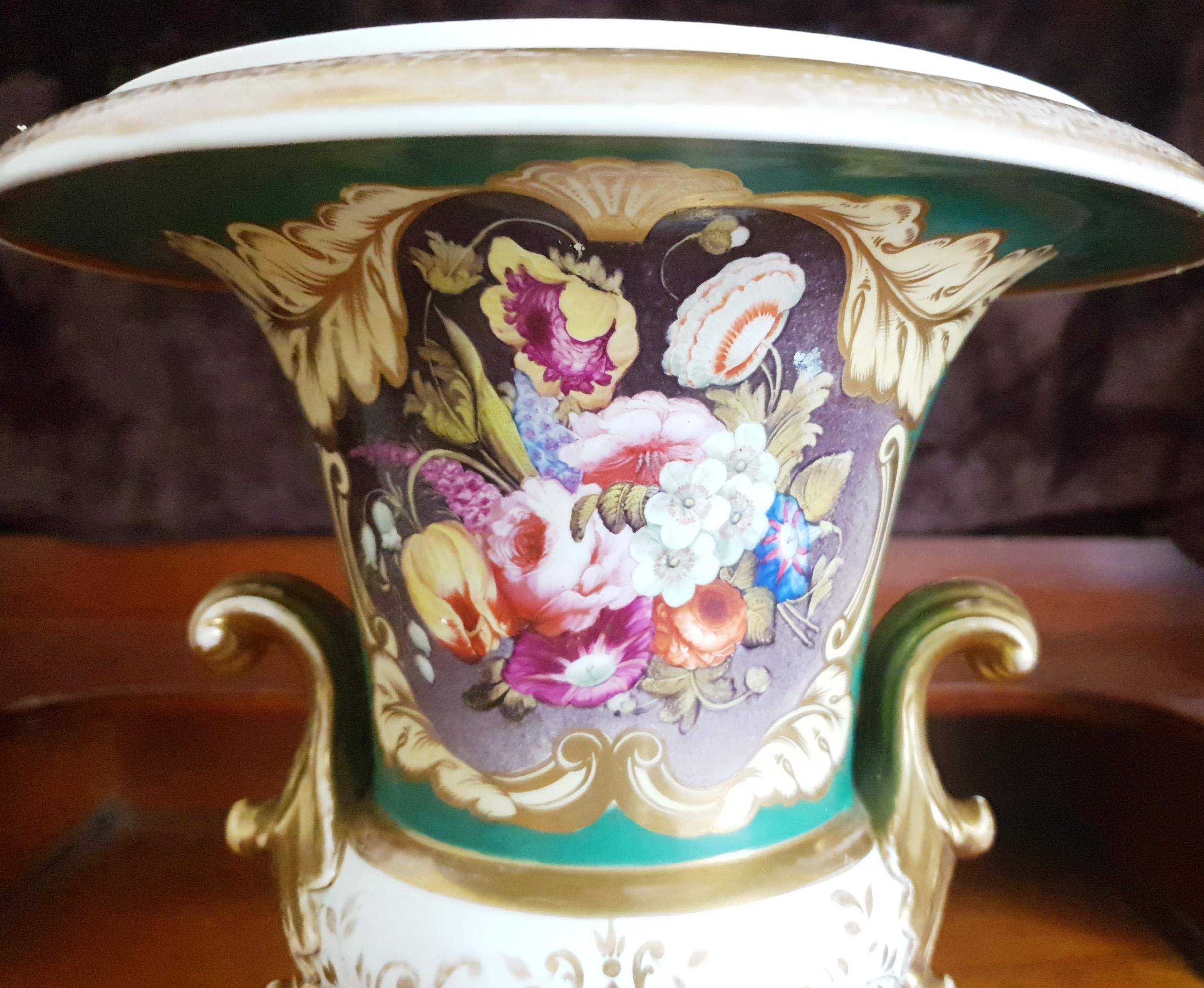 A lovely large Coalport Campana 19th century hand painted vase with gilt turned out handles. The front panel is covered in hand painted blooming summer flowers set within a gilt cartouche on a green ground. A yellow tulip, primulas, pink roses,