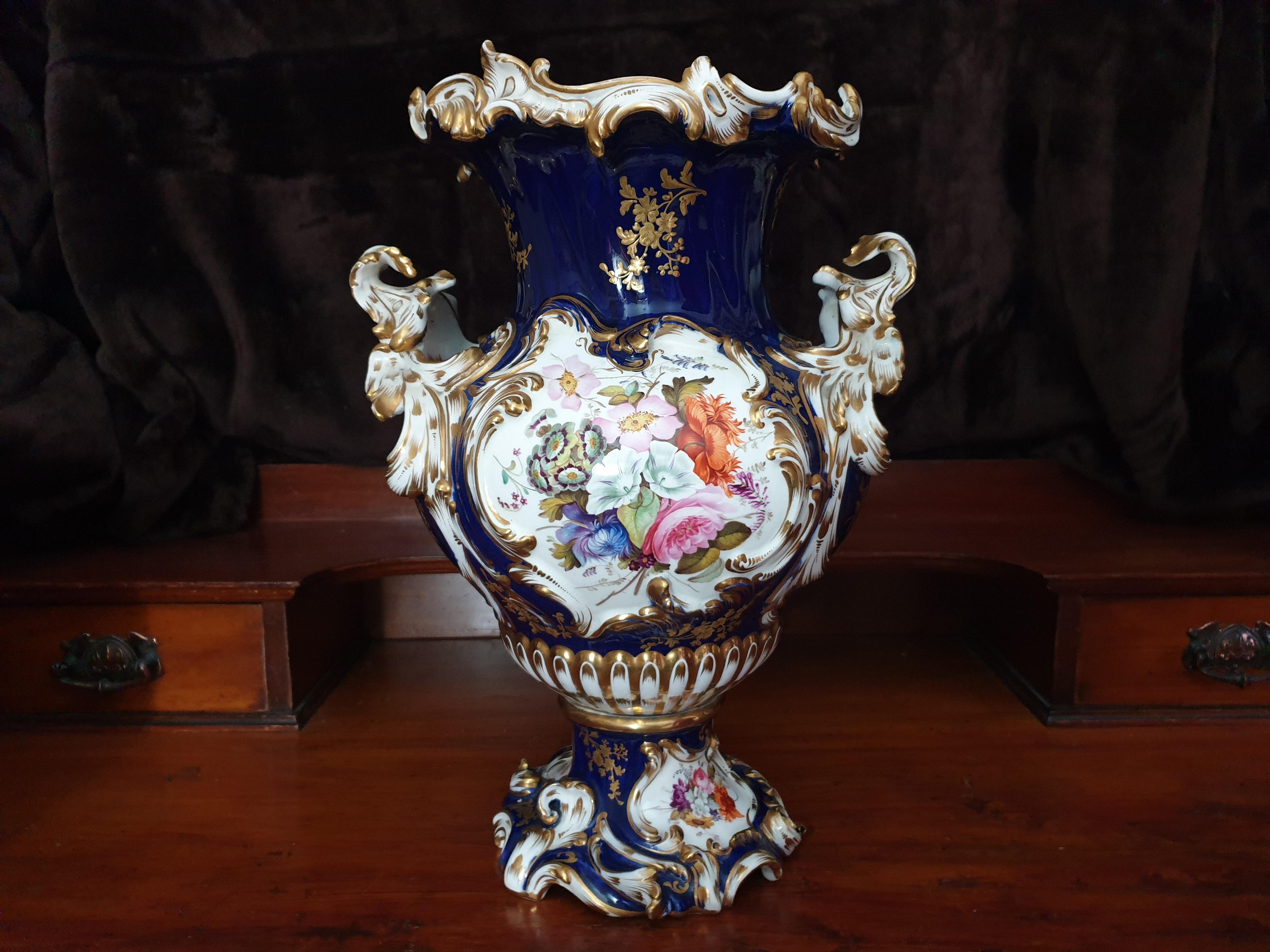 A Coalport Rococo Revival two-handled vase, painted with colourful summer flowers in shaped reserves of raised and gilt C-scrolls and rocaille and Gilt Petals. The gros bleu ground with flowering leafy sprigs in ciselé gilding, conforming rim and