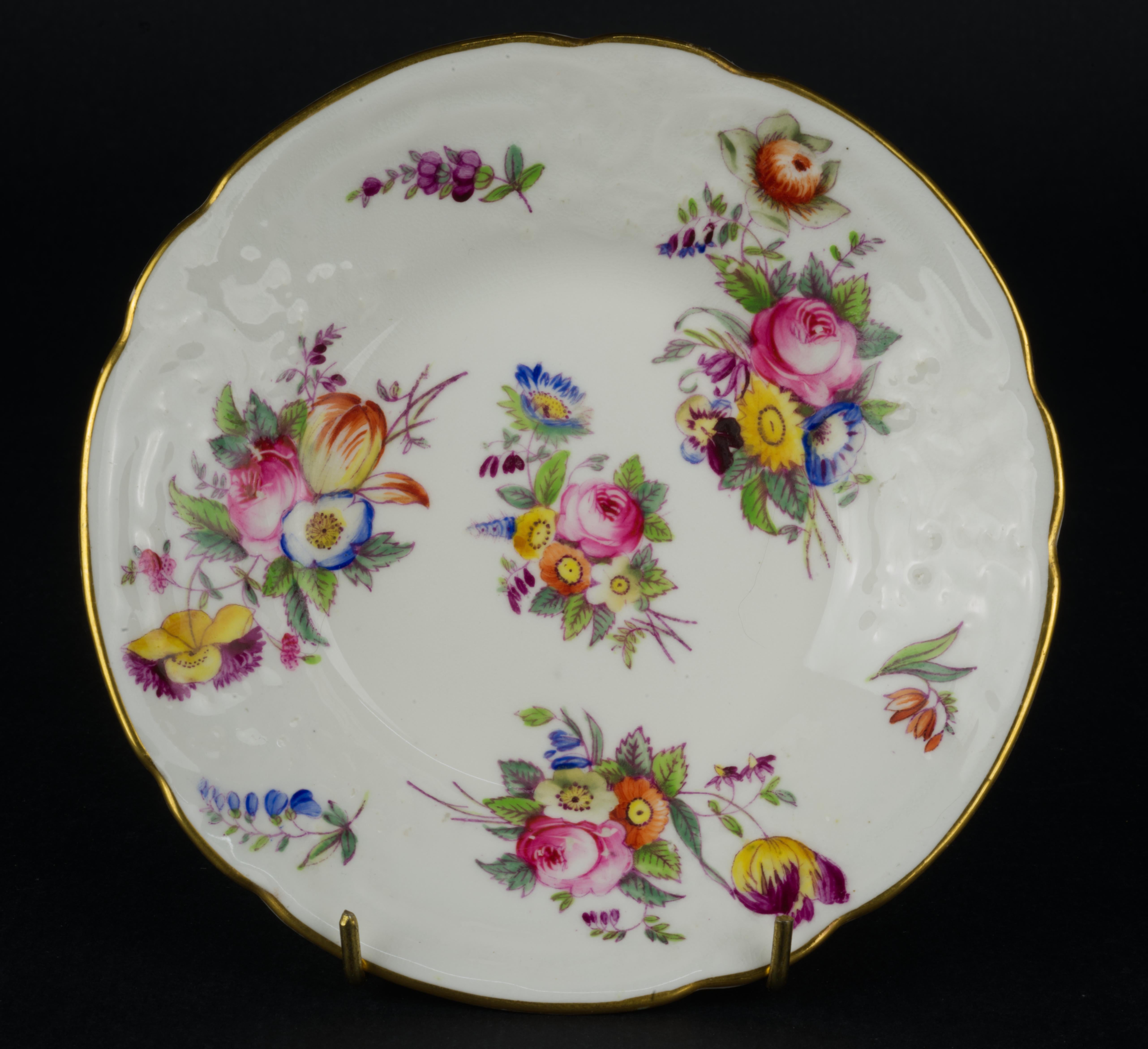  L'ensemble tasse et soucoupe a été fabriqué en Angleterre par Coalport pour Davis Collamore New York en fine porcelaine d'os semi-transparente avec des motifs moulés en relief sur le pourtour de la forme. L'ensemble est peint à la main avec des