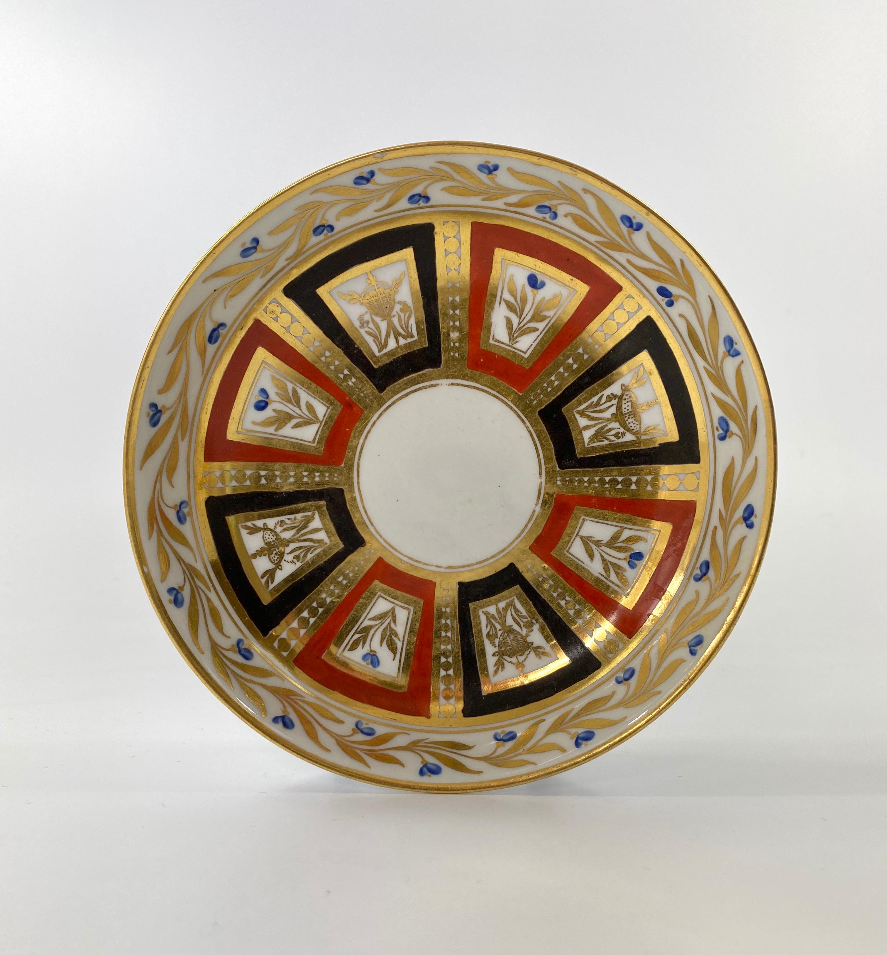 Coalport porcelain coffee can and saucer, c. 1810. Both pieces hand painted with alternating panels of stylised scrolls and flowering plants, in Classical taste. The borders with continuous gilt scroll and blue flowerheads, within gilt