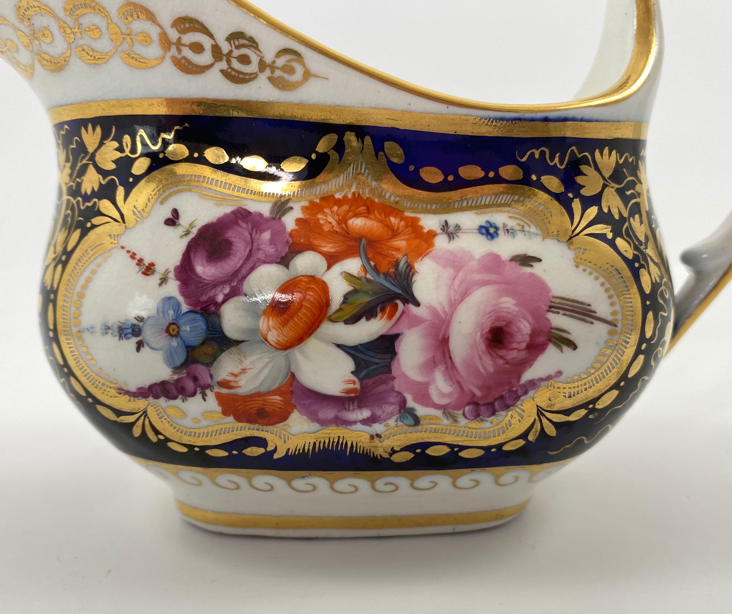 Coalport porcelain cream jug, c. 1830. Hand painted with sprays of flowers, within gilt scroll panels. The cobalt blue ground, decorated with gilt graping vines. Having an angular handles, and decorated in gilt with stylised acanthus