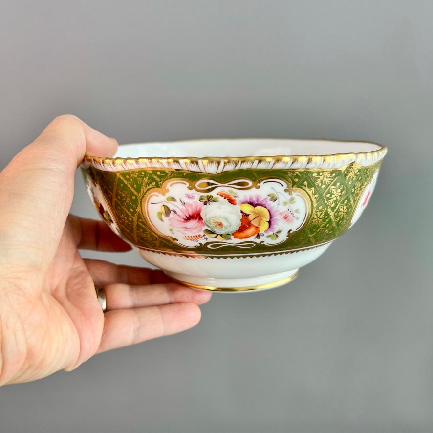 This is a beautiful slop bowl made by Coalport around the year 1820. The bowl has a gadrooned rim, a deep moss green ground with a gilt trellis pattern, and beautiful hand painted flower reserves. There is a very fine flower reserve in the bottom of