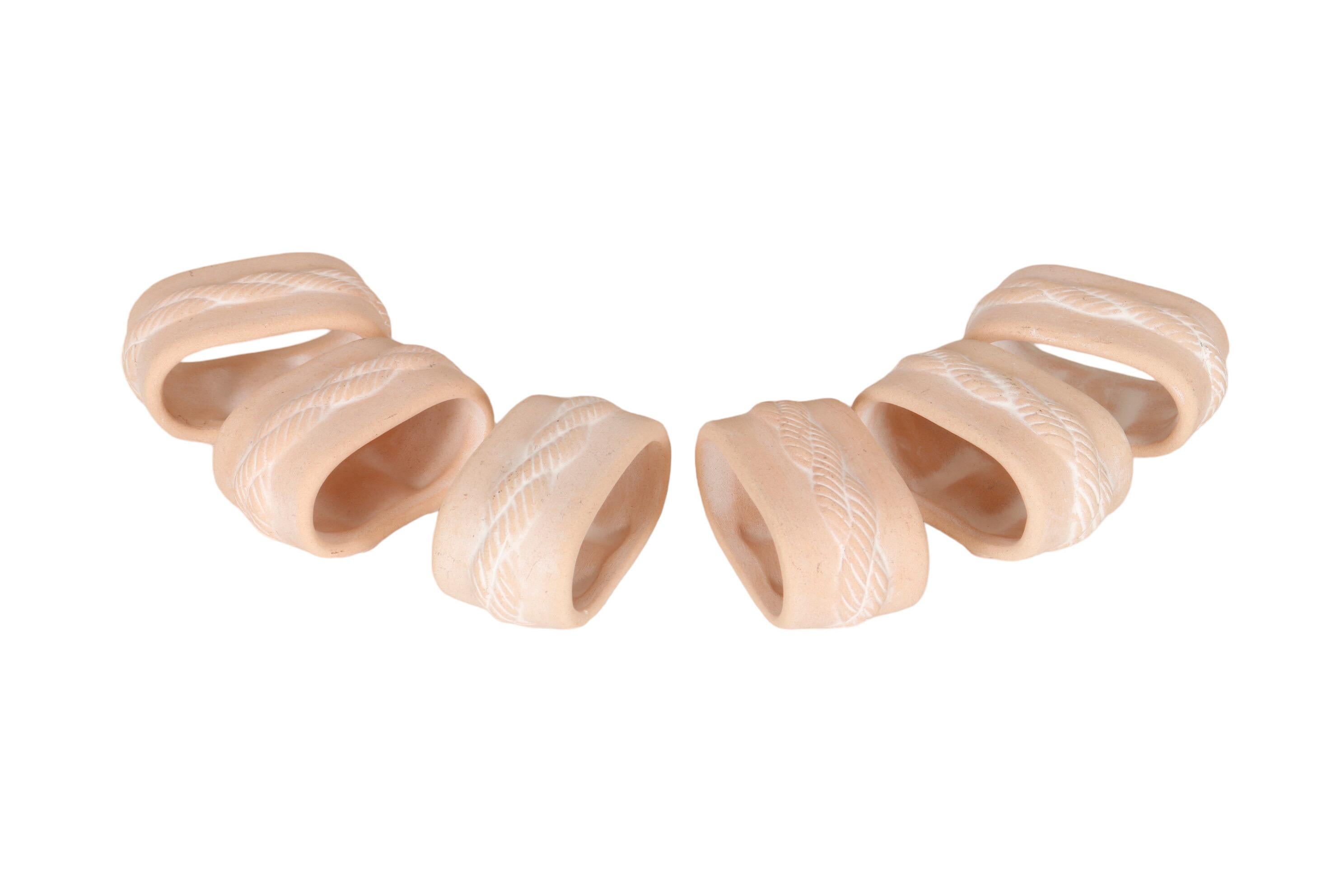 A set of six coastal style napkin rings. Unglazed ceramic in a soft coral color are pressed with a rope twist around the center. Underneath are two feet. Dimensions per napkin ring.
