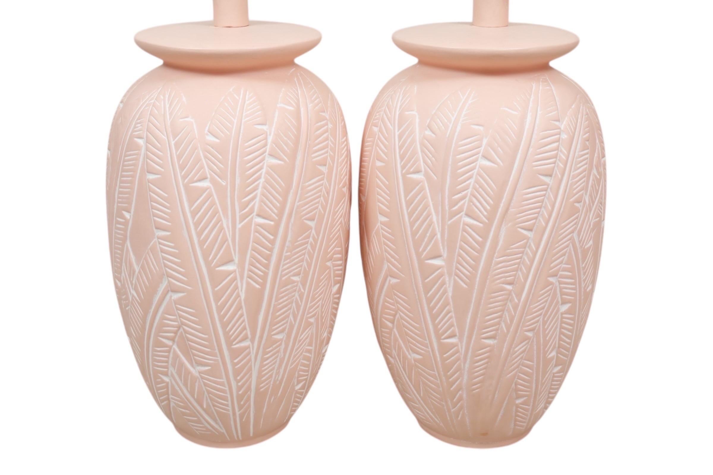 A pair of coastal Sunset Lamp Corp ceramic table lamps. Peach colored vases are decorated with overlapping banana leaves in relief. Maker's label underneath reads “copyright Sunset Lamp Corp”. Each lamp measures 23