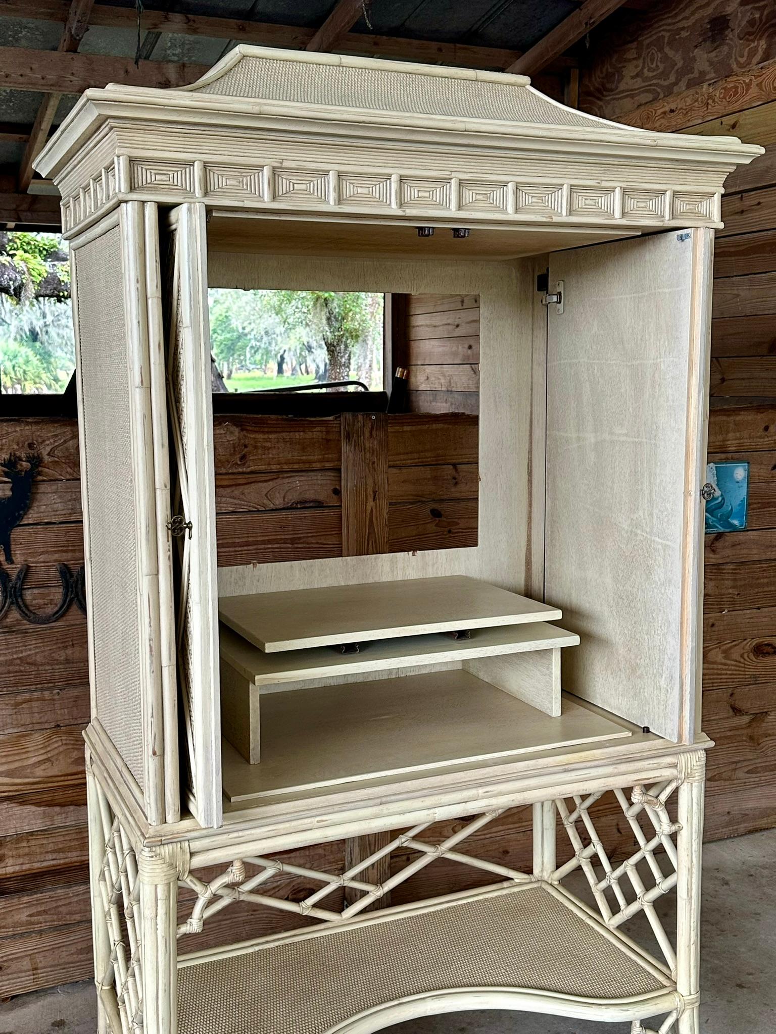 Presenting a stunning woven rattan fretwork Chippendale-style armoire cabinet, featuring an elegant off-white distressed finish and a distinctive pagoda top, perfect for enhancing your space with a touch of sophisticated coastal charm. This