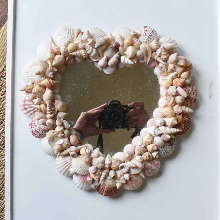 A coastal heart-shaped shell encrusted mirror. This piece would be fabulous in a grouping of similar mirrors, or on its own. Covered in a variety of seashells, this beauty is certainly one of a kind. 

Dimensions:
11.25