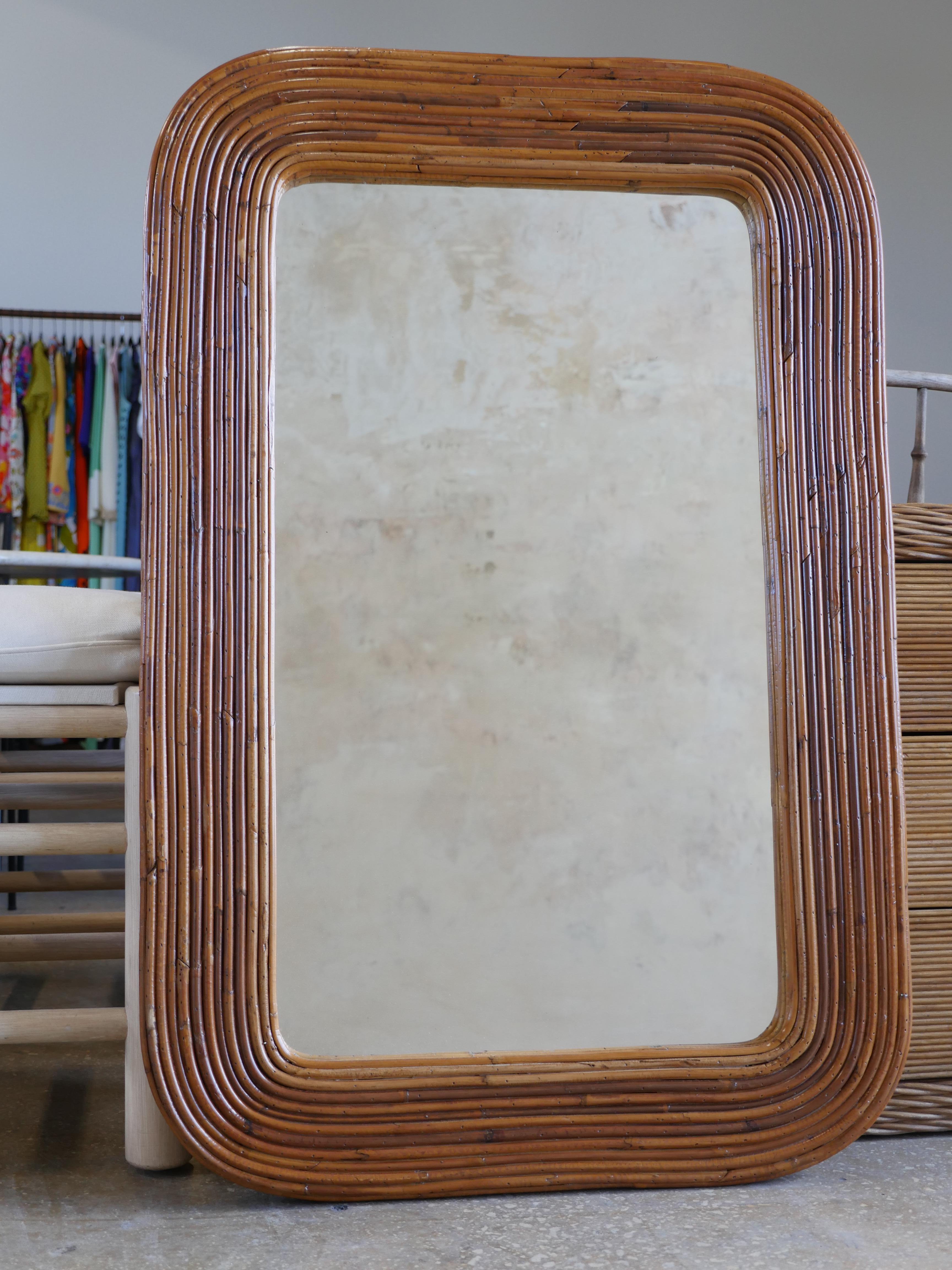 Vintage pencil reed rattan racetrack mirror. The rattan has been refinished in a natural stain, and contains beautiful variations of warm wood tones throughout the mirror.