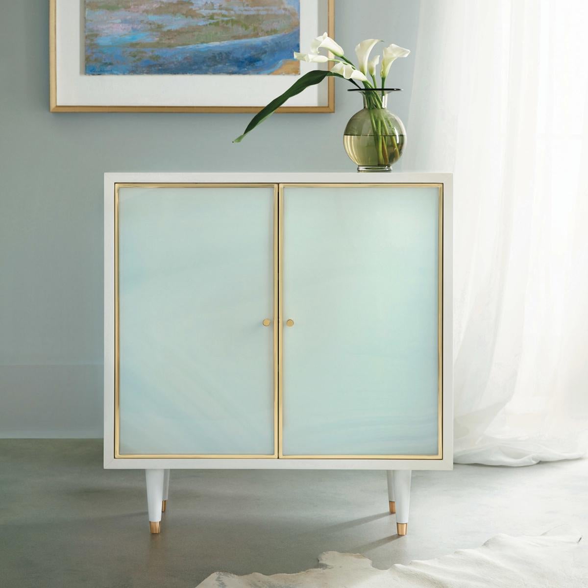 Coastal Sea Glass cabinet. With a white lacquer case and sea glass acrylic door fronts, this two-door cabinet has brass trim framed doors and knob pulls. Raised on turned and tapered legs.

Dimensions: 35