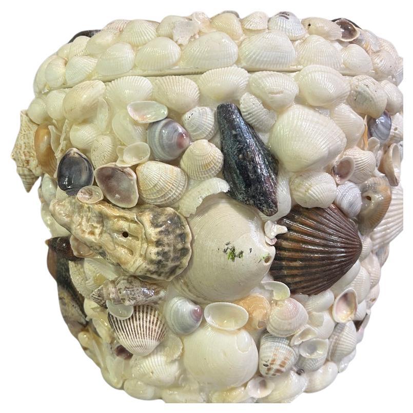 A stunning coastal Sea Shell encrusted ice bucket with a lid. This piece was created in the 1970s and is made of styrofoam. (Which makes it incredibly lightweight.) It is covered in a variety of seashells around the body as well as the lid. The lid