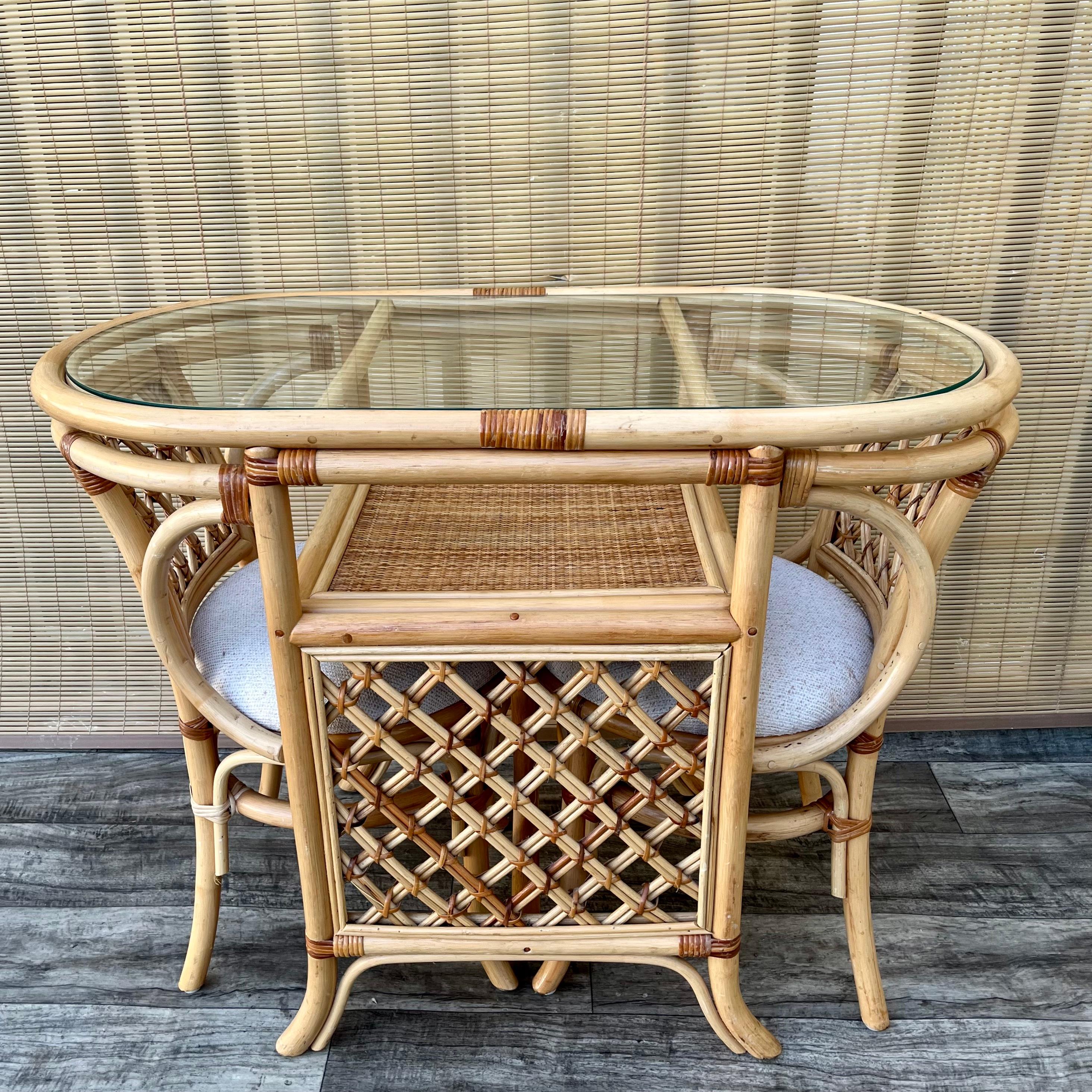 Vintage Coastal Style / Boho Chic Set da colazione e tavolo da pranzo a due posti in vimini e rattan, anni '80 circa.  
Questo grazioso e pratico set da pranzo comprende un tavolo ovale con piano in vetro rimovibile e due sedie che scorrono