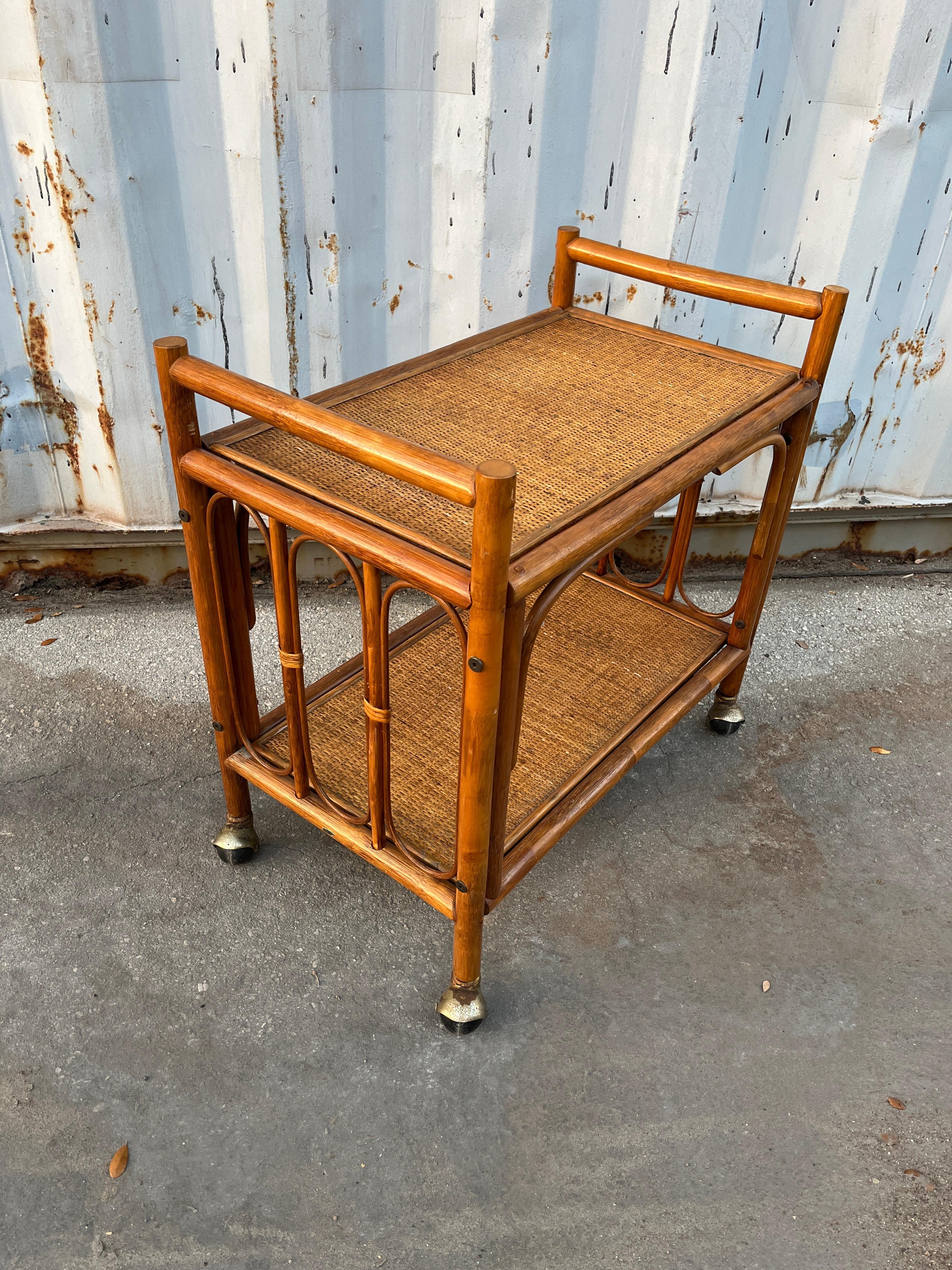 Vintage Boho Chic / Coastal Style Rattan Dry Bar/ Serving Cart in the Franco Albini's Manner. Circa 1970s
Features a two-tiered frame with ornate accents and handles at both sides.
In good original condition with minor signs of wear and age. There