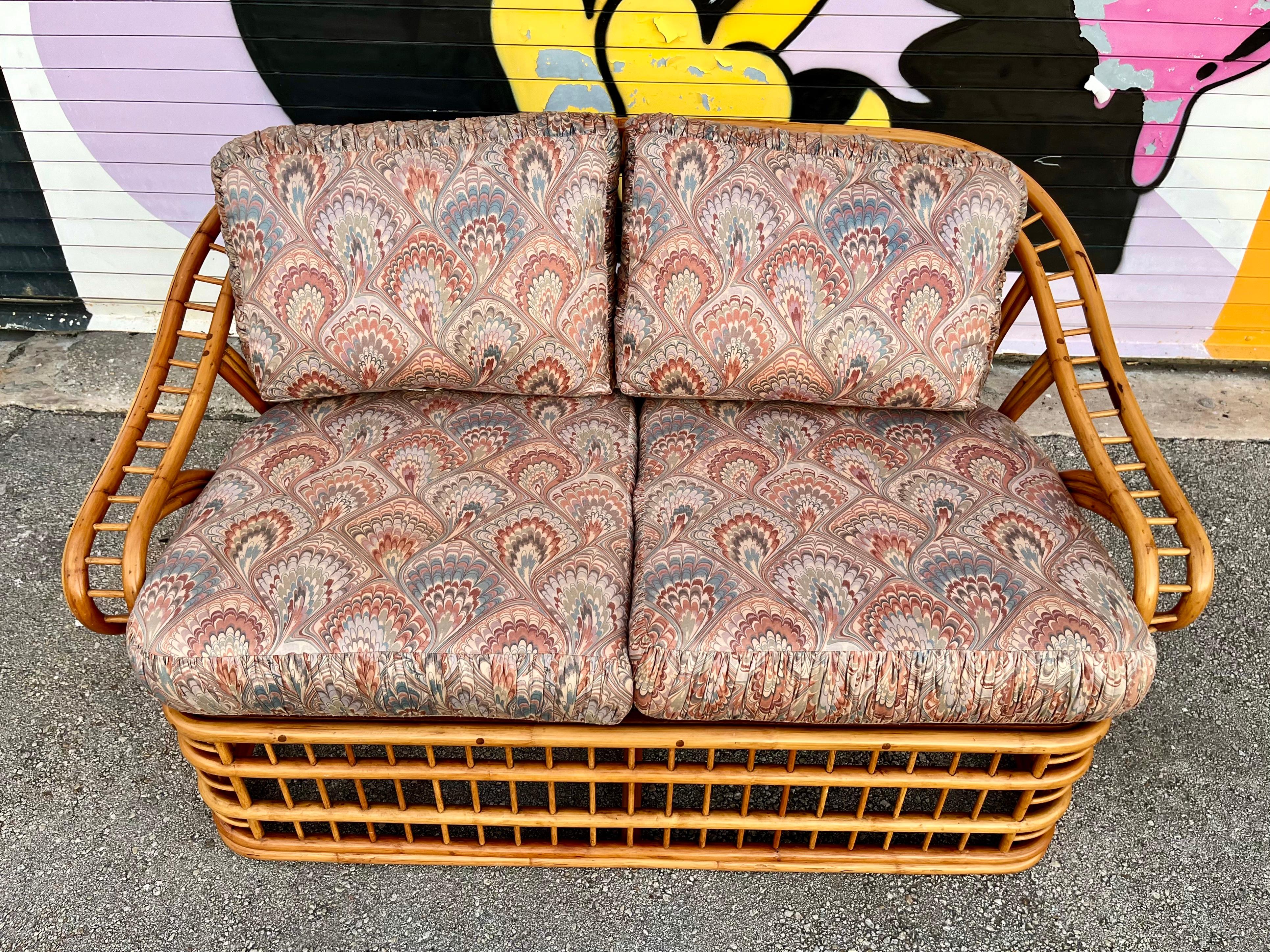 Vintage Coastal Style Rattan Loveseat by Whitecraft Rattan Inc, Miami. FL. Circa 1970s
Features a bent rattan frame with an intricate and dynamic fluid design at the back and armrests. 
In excellent original condition with very minor sings of wear