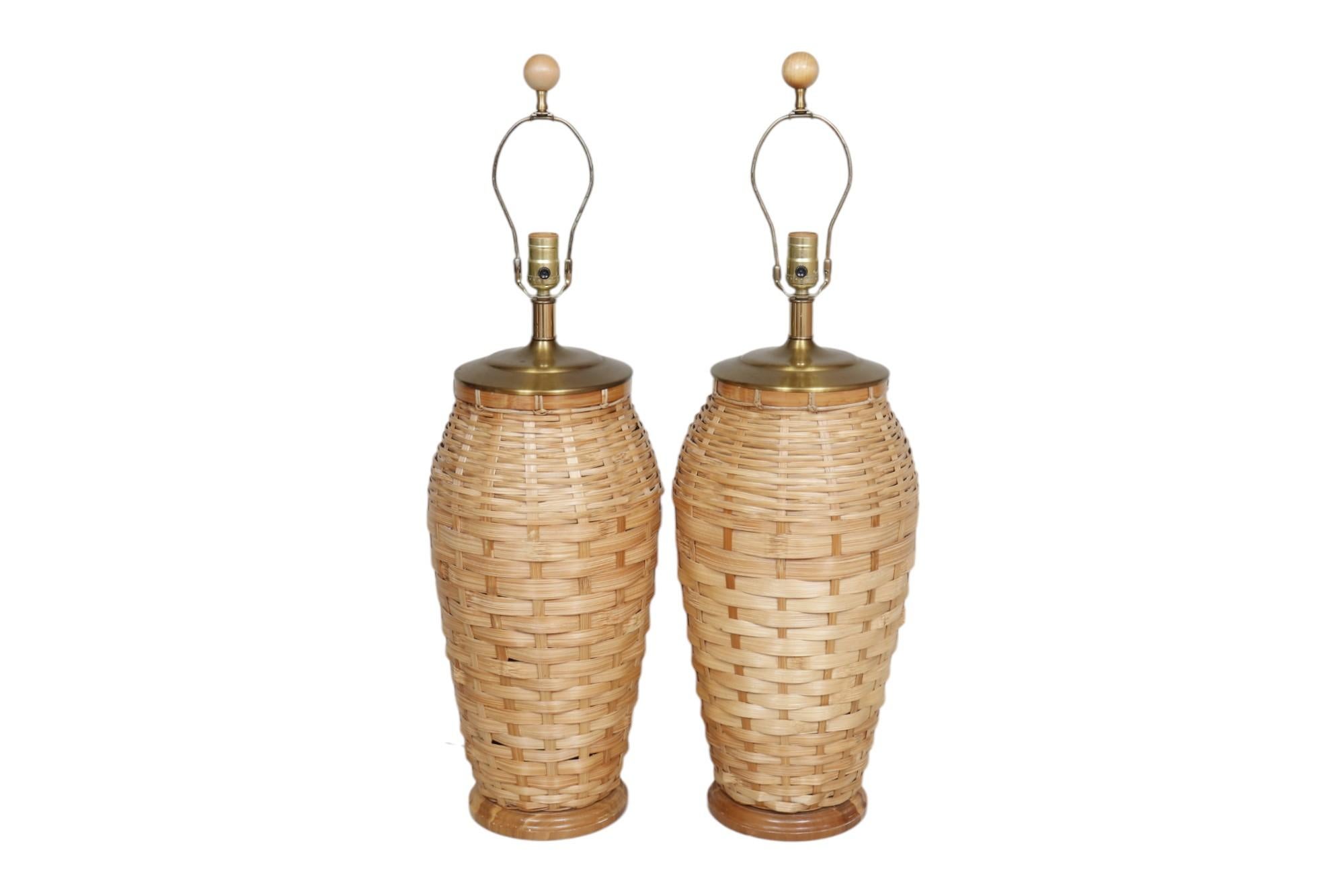 Paire de lampes de table en osier tressé avec abat-jour empire classique en lin. Les vases sont surmontés de capuchons en laiton et reposent sur des bases en bois biseautées. Les harpes sont surmontées de boules en bois assorties. Chaque lampe
