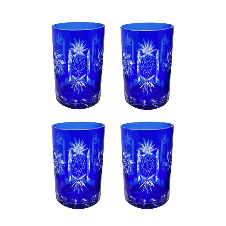 A set of cobalt blue crystal tumblers and pitcher after Baccarat. This lovely blue glass set is cut to clear in geometric lines and shapes. Each of the four tumblers features wheat and leaf carvings with stars and stylized geometric accents. The