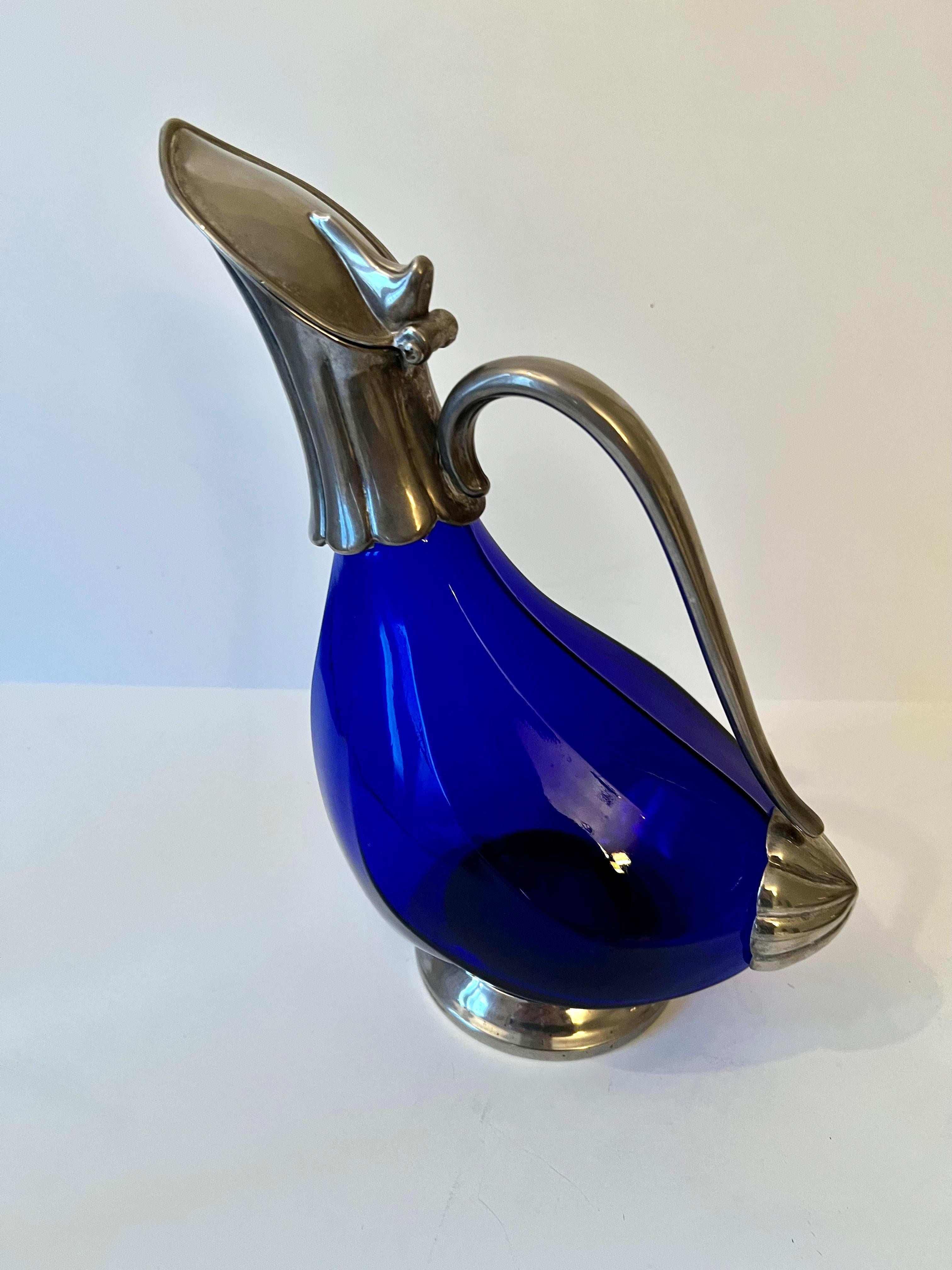 Une belle carafe bleu cobalt avec une base en argent, une poignée et un couvercle à charnière. Le bleu est une couleur étonnante qui s'intègre parfaitement à tout bar ou toute table. En très bon état vintage.