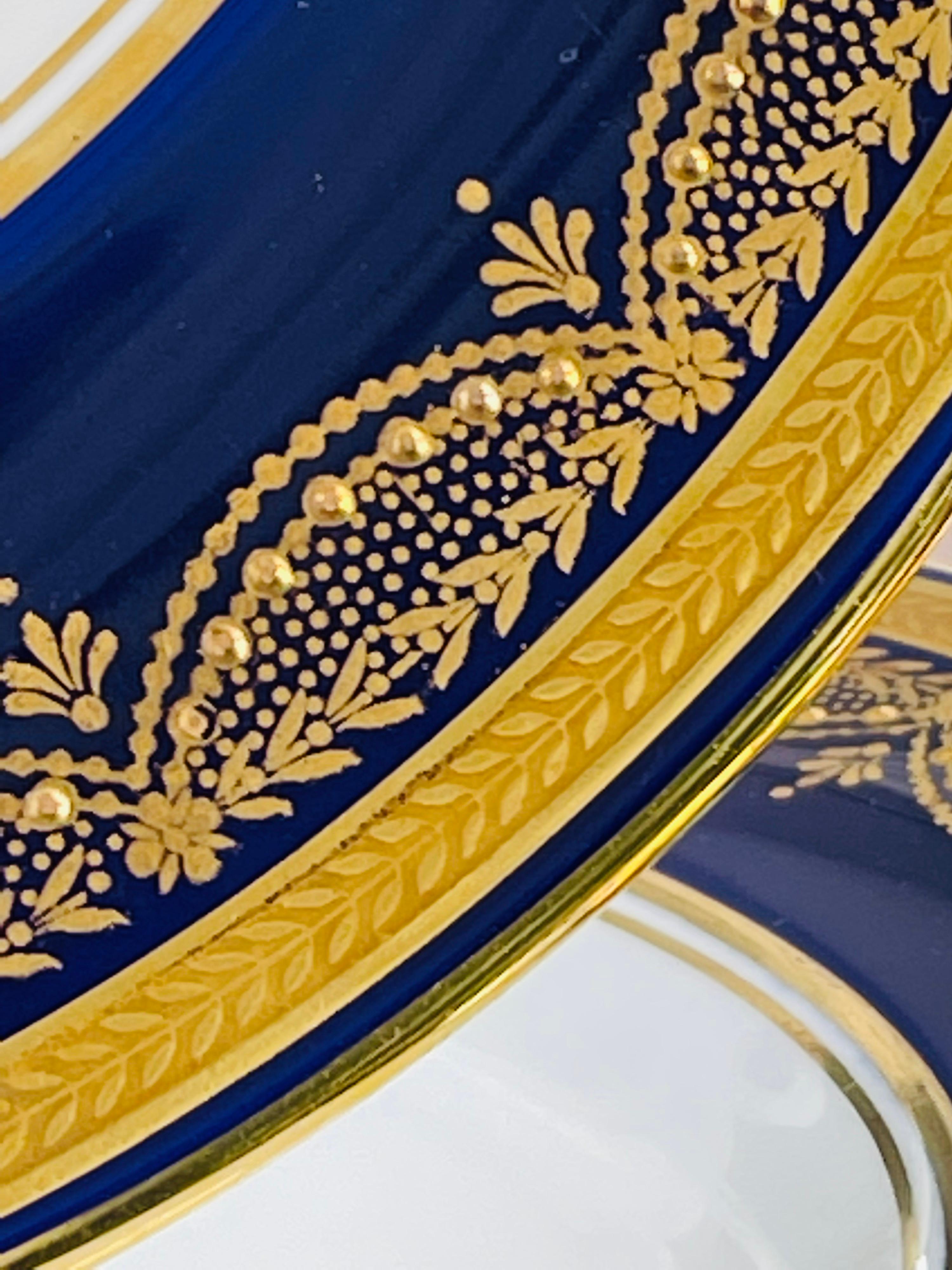 Un ensemble de 12 assiettes à dîner bleu cobalt par Aynsley England. 
Ce magnifique ensemble de Bone China a un bord bleu cobalt avec des contours de feuillage et de l'or en relief 24 carats. 
La marque du fabricant au dos les date d'environ 1939.