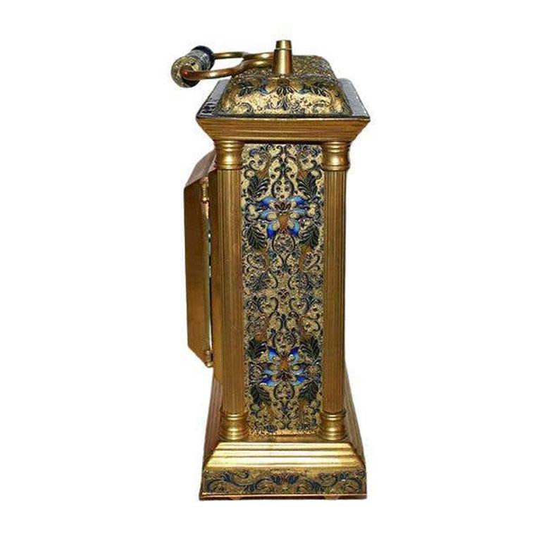A colorful enameled cloisonne carriage or mantle clock. A lovely gold clock with a detailed floral enameled design in cobalt blue, turquoise, pink, and mint green. The piece sits upon four rounded metal legs. The top features a handle with a pink