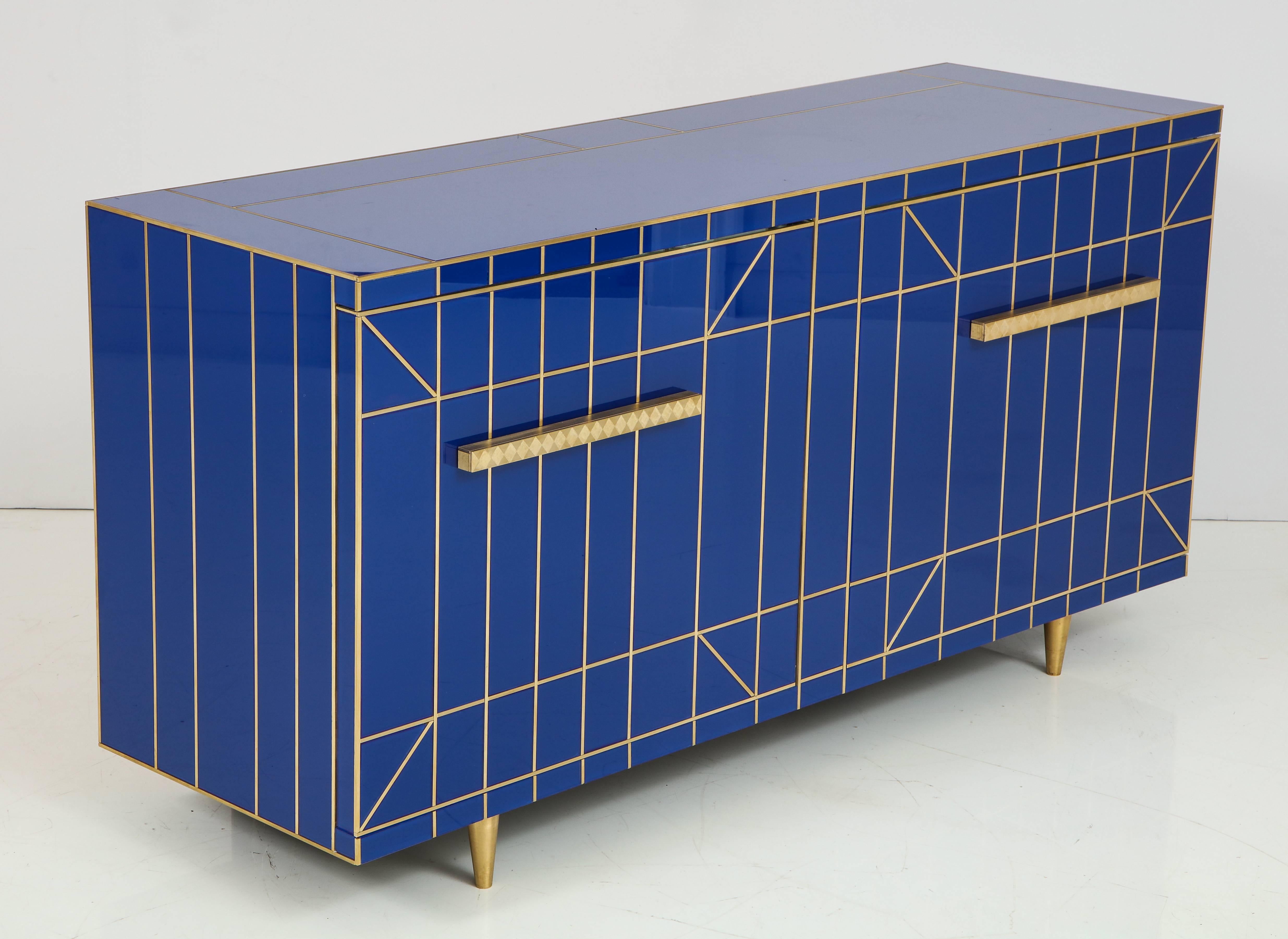 Cobalt blue glass sideboard or credenza with tapered brass legs and brass inlays. Interior is lined in mirror. Two doors open to reveal a large storage area separated by a smaller top level shelf that is clad in mirror. This is a custom piece