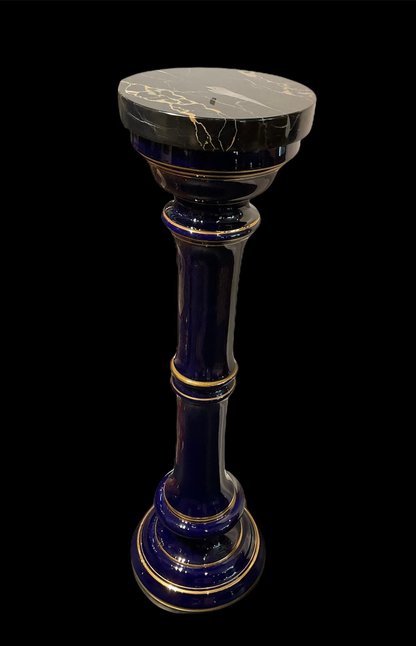 This is a cobalt blue Roman Tuscan shaped column with round black marble top. The column is adorned with several gilt rings around it at different levels from the top to the base.