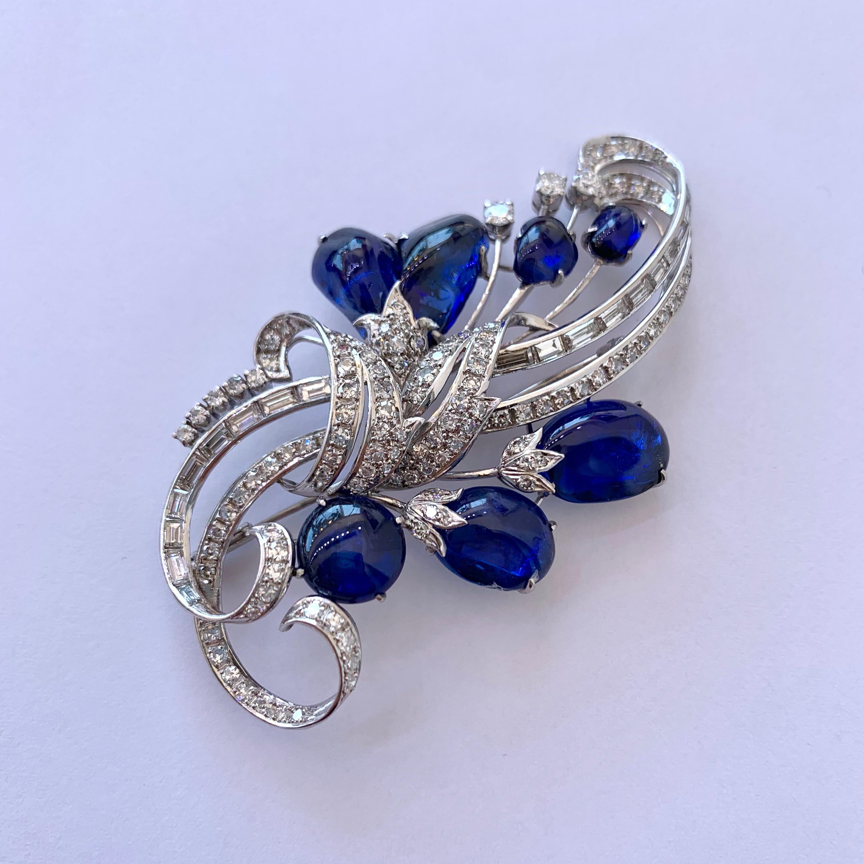 The vibrant blue sapphire and diamond vintage platinum brooch is designed with a floral and ribbon motif, and contains 33cts of vibrant blue tumbled sapphires, and approximately 3.33cts of single cut round and baguette cut diamonds.