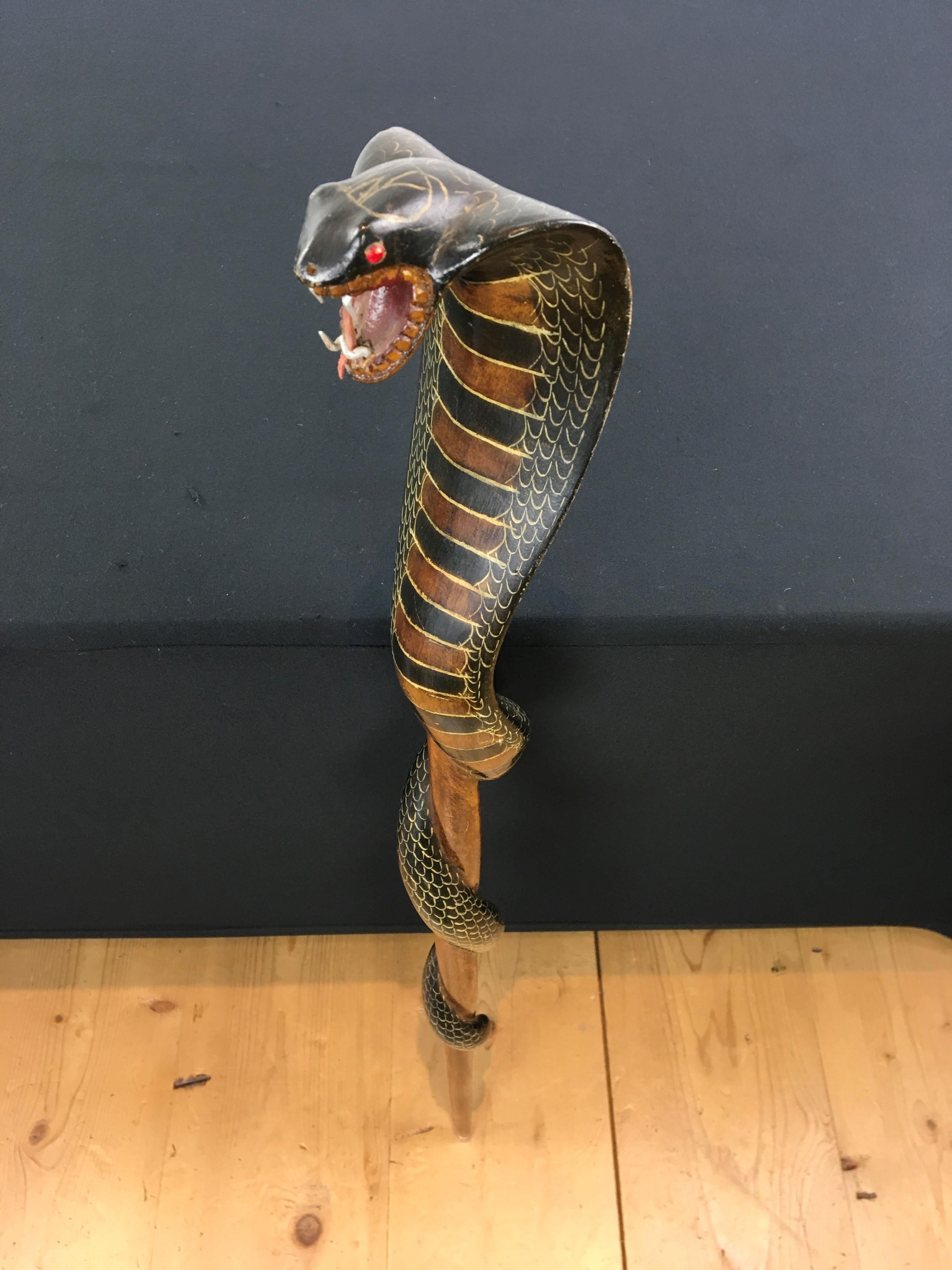 Vintage cobra walking stick. 
A hand- carved wooden walking cane with cobra or snake head as handle. The body of the snake is wrapped around. Beautiful brown and black colors with painted scales. The snake has his mouth open, has teeth and a