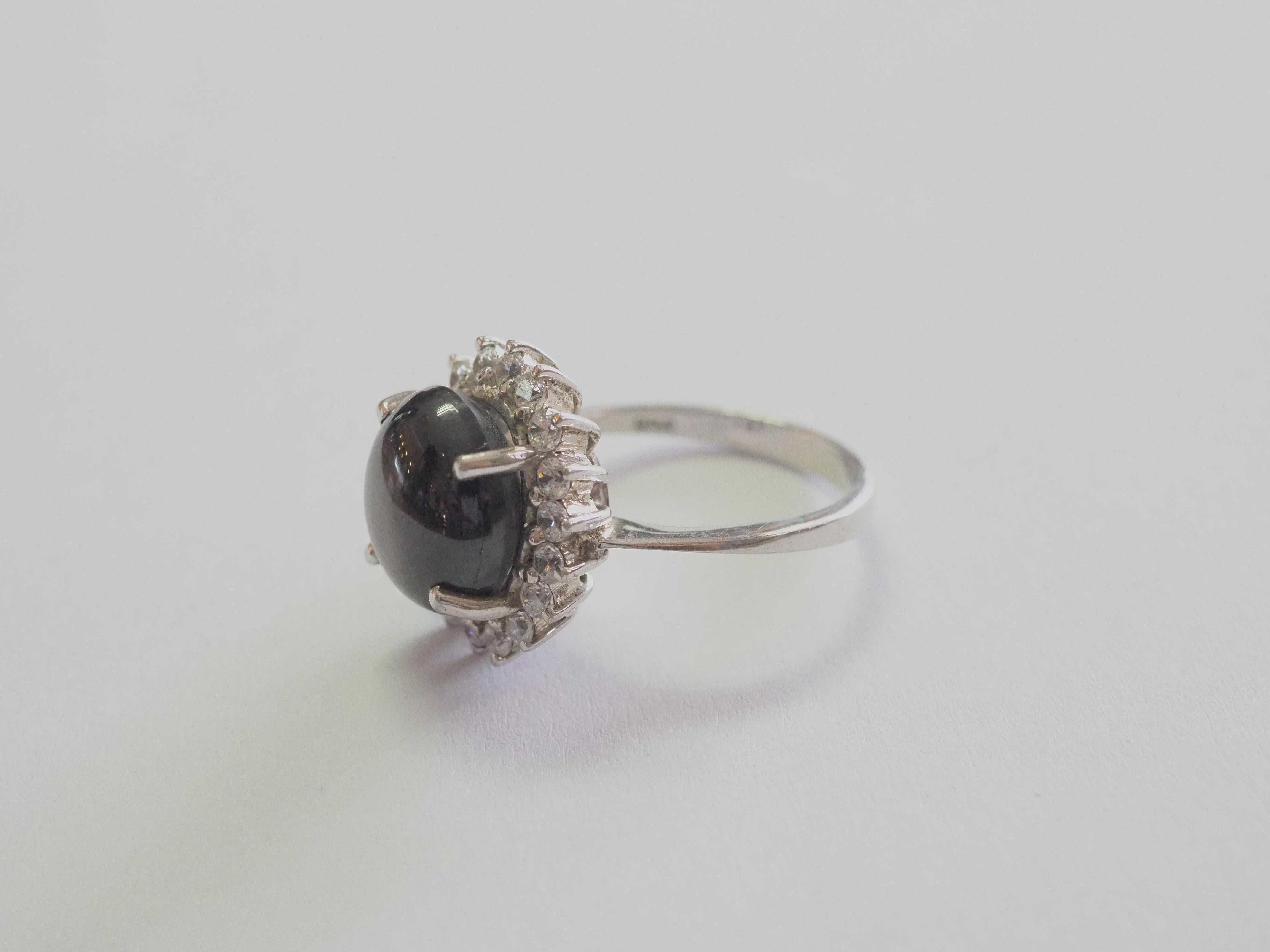 This ring is a beautiful cocktail ring in solid sterling silver. The ring is decorated by natural cabochon black star sapphire prong set in the middle. The brilliant white stones are cubic zirconia. The lindy star will show when shone light directly