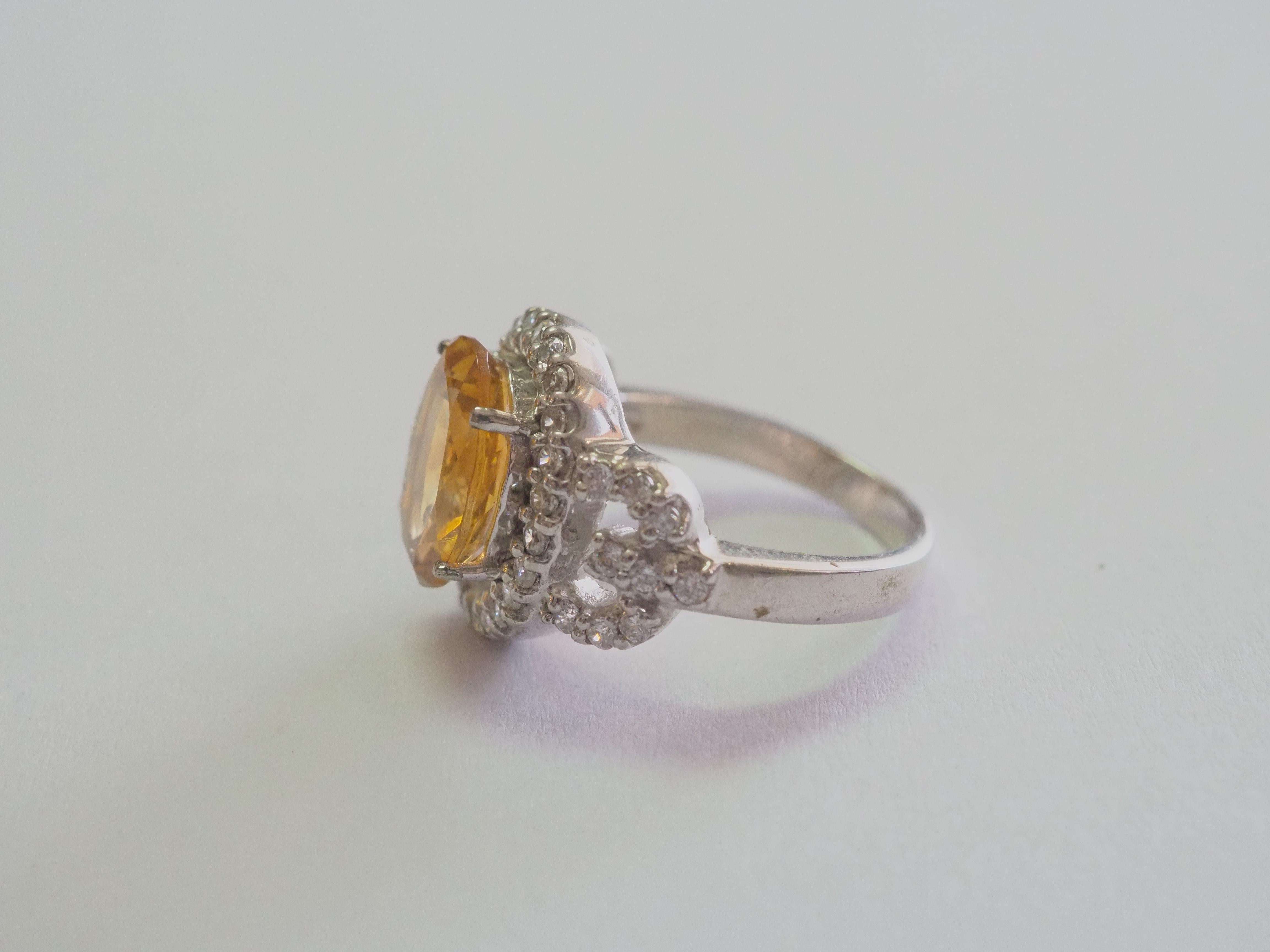 This ring is a beautiful and elegant cocktail ring in solid sterling silver. The ring is decorated by oval citrine prong set in the middle. The brilliant white stones surround the yellow gem are cubic zirconia. The citrine is very widely popular due