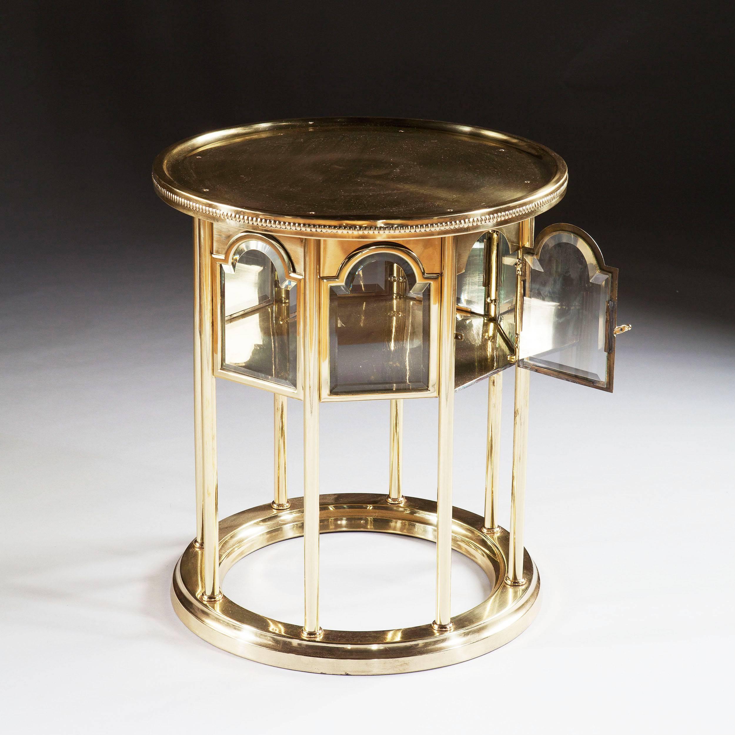 A mid-20th century hand-beaten and polished brass circular cocktail table with a reeded edge to the top above stunning glazed vitrine with a door and bevelled glass, supported on columns.
France, circa 1950

Measures: Height 24 ins (61