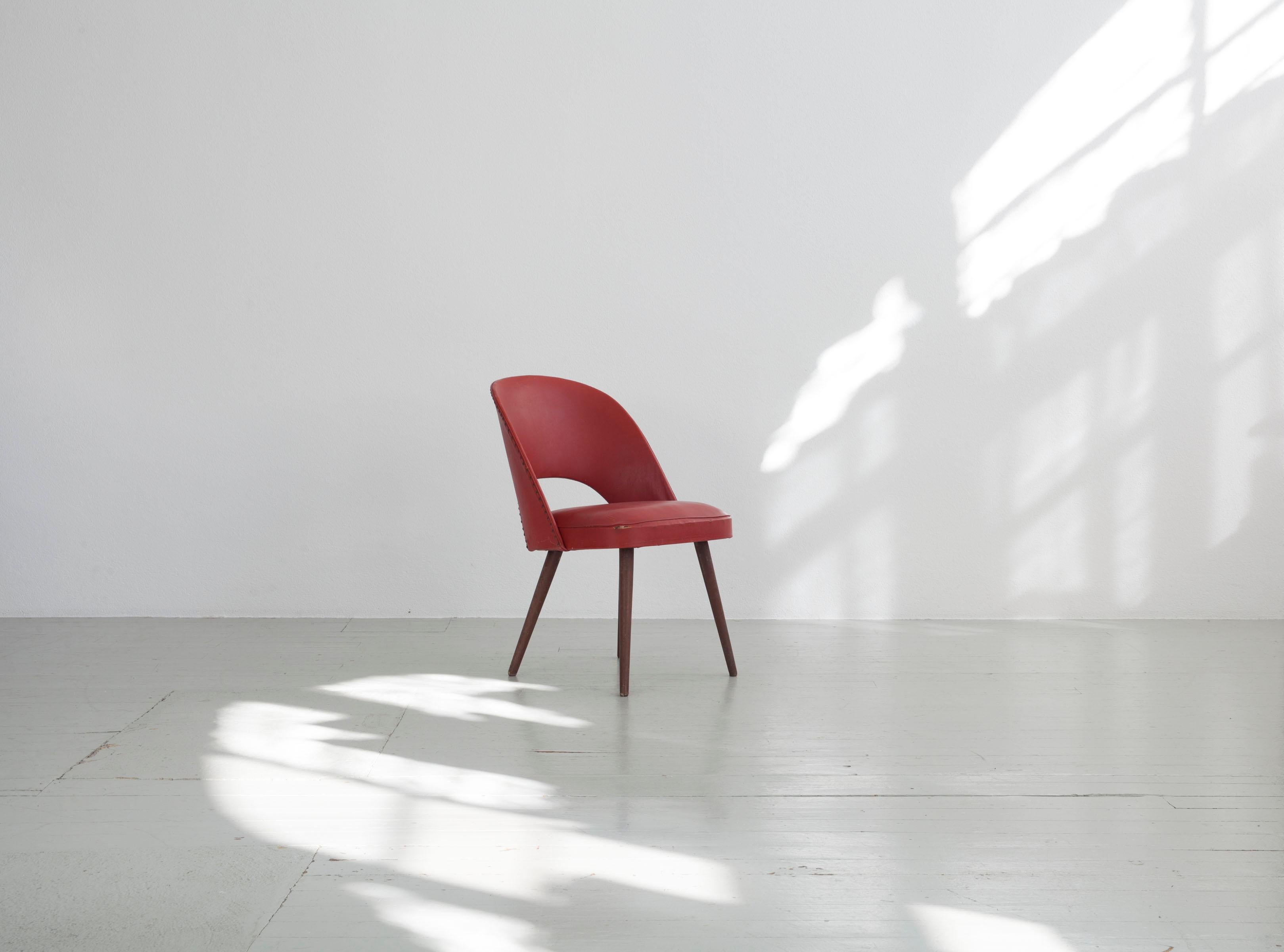 The relatively small cocktail chair covered with a firm vinyl cover, the seams of which are stabilised by a piping strip. The backrest is not only decorated with upholstery nails in the lower arch, but also reinforced. The chairs stand sturdily on