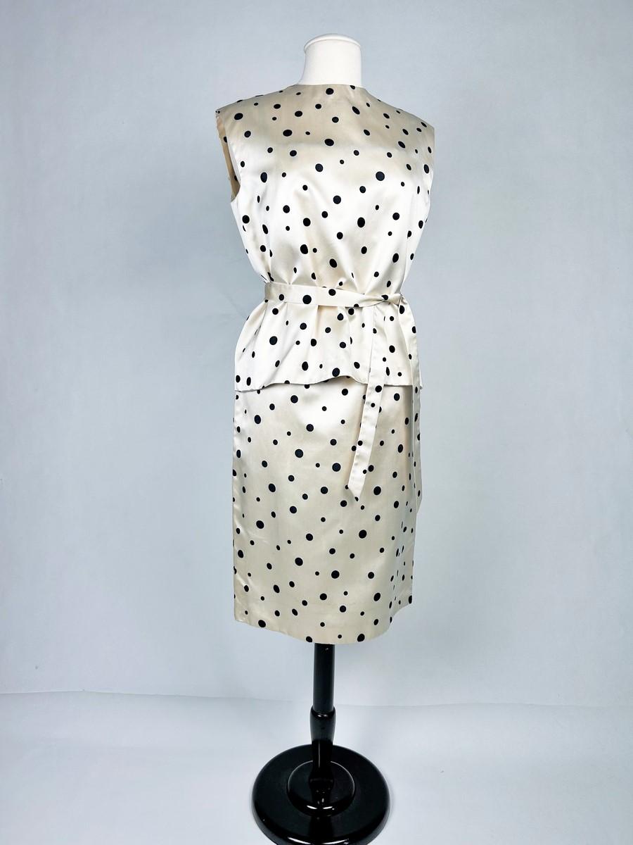 CIRCA 1960-1965
Frankreich
Cocktail- oder Gesellschaftskleid aus gepunktetem Seidensatin eines nicht näher bezeichneten Couture-Studios aus den 1960er Jahren. Der Hintergrund ist ein atemberaubender cremefarbener Satin, der mit einem Samtplumetis