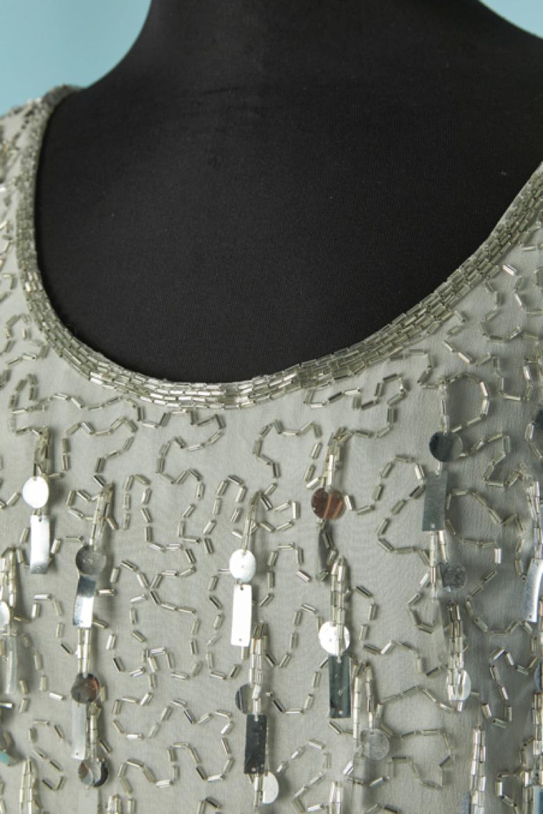 Abito da cocktail con perline e paillettes argentate su una base di seta grigia. Non c'è l'etichetta della composizione del tessuto per la fodera, ma probabilmente si tratta di acetato o rayon. 
Chiusura con zip invisibile e gancio sulla parte